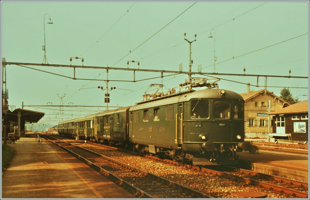 Die Re 4/4 I 10041 mit einem Schnellzug von Biel/Bienne nach Delmont wartet in Grenchen Nord auf die Abfahrt. 
August 1984