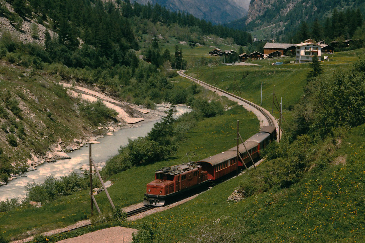 BVZ: Ein gemischter Zug mit der HGe 4/4 15 auf der Fahrt nach Zermatt im Juni 1986. Nebst zwei Wagen mit offenen Blattformen wurde noch ein Post- und Gterwagen mitgefhrt. Zu dieser Zeit gab es auch noch die speziellen hlzernen Fahrleitungsmasten.
Foto: Walter Ruetsch 