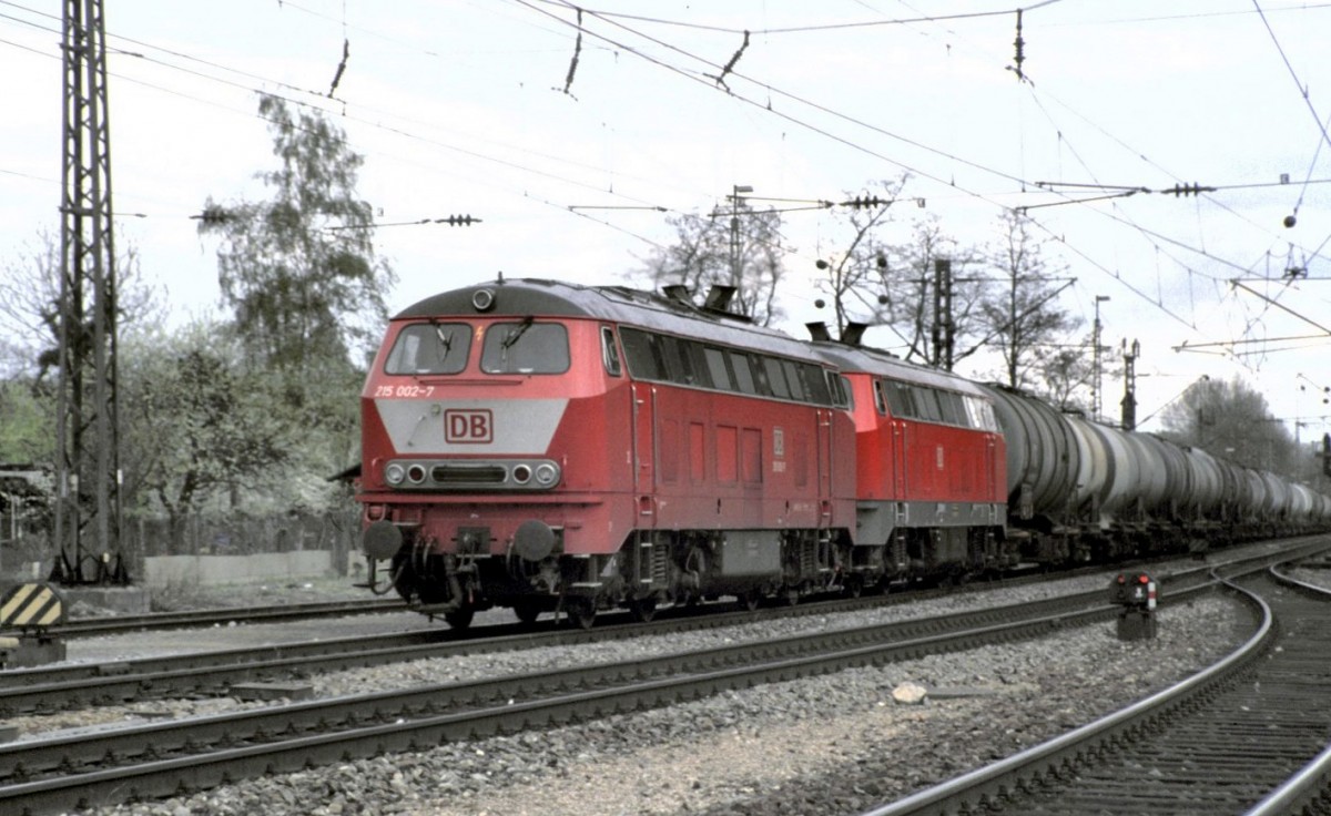 Das bunte Leben der 215 001-9. Als führende Zugmaschine ist die 215 002-7 zu sehen mit  Lätzchen , während die 215 001-9 bereits die Farbe Neurot mit dem weißen Streifen an der Front hat. Der Zug besteht aus leeren Tankwagen aus dem Allgäu, bei Neu-Ulm im Juli 1998. (Diascan)