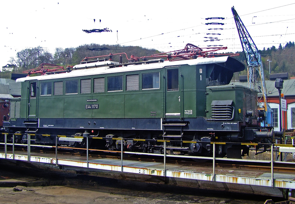 Die E 44 1170, ex DB 145 170-7, ex E 44 170W, wird am 12.04.2010 auf der Drehscheibe im Südwestfälische Eisenbahnmuseum in Siegen präsentiert. Leider eine meiner wenigen brauchbaren Aufnahmen von ihr.

Die Lok wurde 1944 von Krauss-Maffei in München unter der Fabriknummer 25575, der elektrische Teil ist von SSW (Siemens-Schuckertwerke), und wurde an die Deutschen Reichsbahn als E 44 107W geliefert. 

Die von der Deutschen Reichsbahn beschafften Lokomotiven der Baureihe E 44 wurden als Universalloks für den Personen- und Güterverkehr in Süd- und Mitteldeutschland eingesetzt. Die Elektrolokomotiven der Baureihe E44 waren die ersten E-Loks in Deutschland, die in größerer Stückzahl (187 Stück) gebaut wurden. Diese von den Siemens-Schuckertwerken als Universalloks konzipierten Lokomotiven prägten von 1933 bis in die 80er Jahre den Eisenbahnverkehr hauptsächlich in Süd- aber auch in Mitteldeutschland aufgrund ihrer Robustheit und Zuverlässigkeit. 1984 rollte letzte E44 der DB aufs Abstellgleis.
Einige Exemplare der E44 wurden für den Betrieb auf der steigungsreichen Höllentalbahn mit einer zusätzlichen elektrischen Widerstandsbremse ausgerüstet. Von den hiervon bestellten 40 Lokomotiven wurden zwischen 1943 und 1951 32 Stück gebaut.

Diese Loks wurden mit einem „W“ nach bzw. später mit einer „1“ vor der Loknummer gekennzeichnet, wie diese Lok hier (E44 170W, E44 1170) und ab 1968 als DB-Baureihe 145 bezeichnet. Die E44 1170 stand von 1944 bis 1983 im Dienst der Deutschen Bundesbahn, wobei sie die längste Zeit in Freiburg beheimatet war. Nach ihrer Ausmusterung war sie lange Zeit betriebsfähige Museumslok des Bw Freiburg und wurde regelmäßig vor Sonderzügen im Höllental und auf der Dreiseenbahn eingesetzt. 1996 wurde sie endgültig abgestellt und 2002 nach Siegen zu den Eisenbahnfreunden Betzdorf abgegeben. Seit 2010 ist sie nun im Fahrzeugbestand der IG 3seenbahn.

Die E 44 stellen einen Meilenstein der E-Lokentwicklung dar, denn hier wurde erstmals bei einer größeren Streckenlokomotive auf Vorlaufachsen und Stangenantrieb verzichtet. Insgesamt wurden 187 Maschinen gebaut, von denen jedoch etliche durch Kriegshandlungen einen Totalschaden erlitten und deshalb ausgemustert werden mussten. Die Mehrzahl der Lokomotiven kam zur Deutschen Bundesbahn. Diese baute sogar sieben Loks nach. Die DB rüstete mehrere Maschinen für den Wendezugbetrieb aus, kenntlich gemacht durch ein G hinter der Loknummer. Die E 44 mit elektrischer Bremse wurden durch ein W hinter der Loknummer kenntlich gemacht. 

TECHNISCHE DATEN:
Spurweite: 1.435 mm (Normalspur)
Achsformel:  Bo’Bo’
Länge über Puffer:  15.290 mm
Drehzapfenabstand: 6.300 mm
Drehgestellachsstand: 3.500 mm
Treibraddurchmesser : 1.250 mm
Eigengewicht: 77,2 t
Radsatzfahrmasse: 19,5 t
Höchstgeschwindigkeit:  90 km/h
Stundenleistung:  2.200 kW
Dauerleistung: 1.860 kW
Anfahrzugkraft: 196 kN
Stromsystem:  15 kV 16⅔ Hz
Anzahl der Fahrmotoren:  4
Antrieb: Tatzlager-Antrieb

