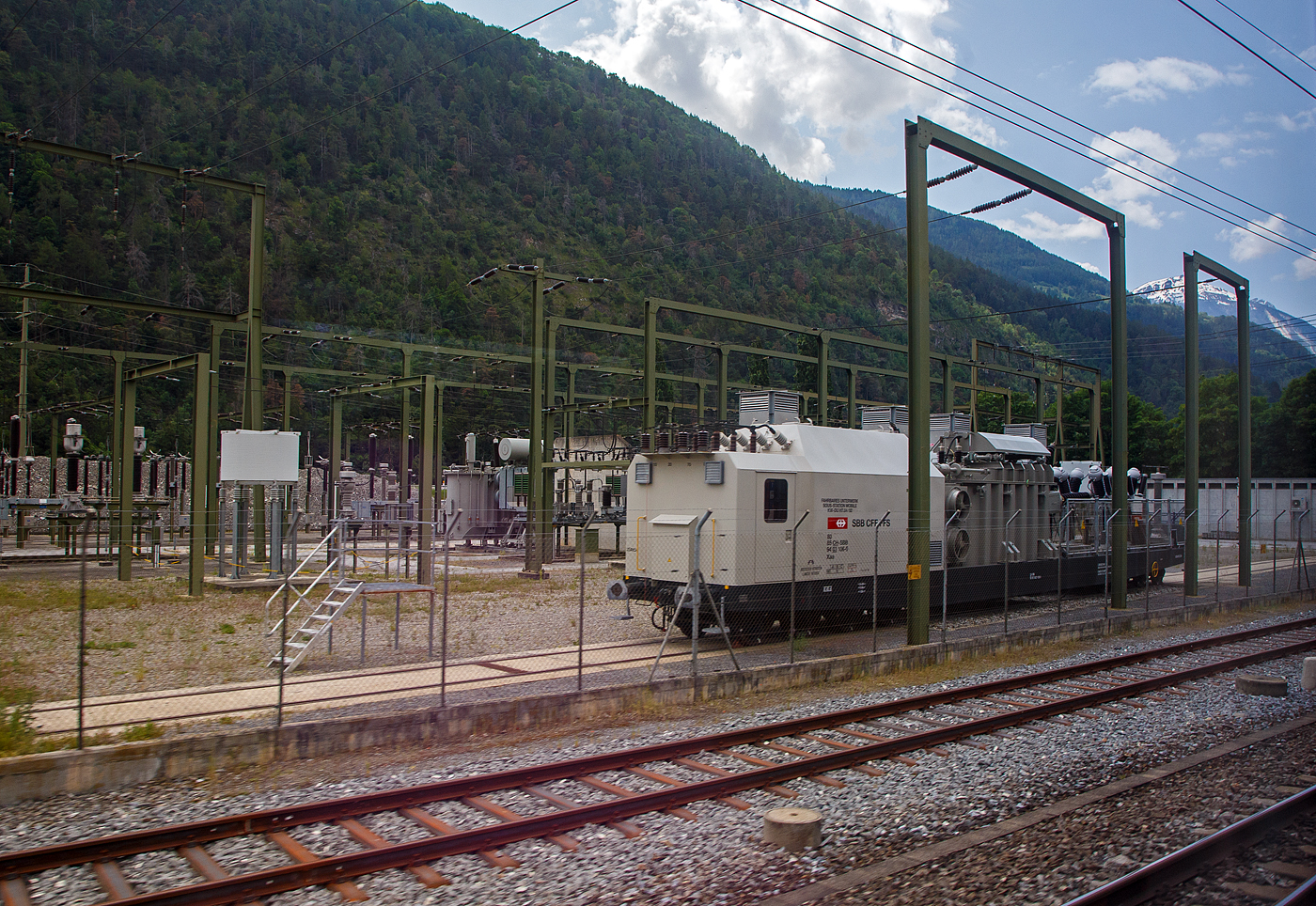 Achtachsiges SBB Fahrbares Unterwerk, Sous-Station Mobile, KW-DU H7.84/92, Xaa 80 85 94 03 106-0 CH-SBB, der SBB - Schweizerischen Bundesbahnen, ex Xa 30 85 98 00 206-x CH-SBB, am 28.05.2023 bei Gampel-Steg/Wallis (Industriezone Schnydrigen), aufgenommen aus einem Zug heraus. 

Ein fahrbares Unterwerk ist ein Umspannwagen bzw. Transformatorwagen mit Hochspannungsschaltanlage. Fahrbare Unterwerke werden insbesondere bei den SBB häufig eingesetzt. Die SBB betreiben ein eigenes Hochspannungsnetz mit einer Frequenz von 16,7 Hertz.

Von dieser dritten Serie (Xa 30 85 98 00 206 bis 209, ab 1991 umgezeichnet in Xaa 80 85 94 03 106 bis 109) Fahrbares Unterwerk wurden 4 Wagen 1985  von der Ferriere Cattaneo SA gebaut. Die 140 t und ca. 24,5 m langen Wagen laufen auf zwei vierachsigen Tiefladewagen-Drehgestelle SBB TLW 52, diese haben einern Achsstand 3 x 1.500 mm, der Laufraddurchmesser beträgt 850 mm (neu).