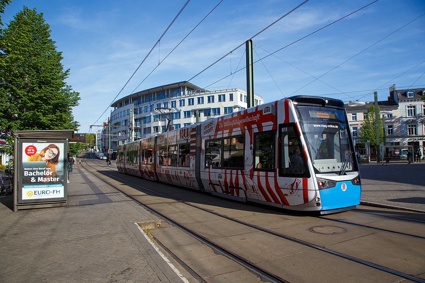 Der 6N2 Niederflur-Multi-Gelenktriebwagen 611, ein Vossloh Tramlink der RSAG (Rostocker Straßenbahn AG) hat am 14 Mai 2022 die Station Doberaner Platz erreicht.

Der 100porzentige Niederflur-Einrichtungs-Triebwagen wurde 2014 von Vossloh Espana (seit 2016 Stadler Rail Valencia), mit der Elektrischen Ausrüstung Vossloh Kiepe (Düsseldorf), gebaut und an die RSAG geliefert.

Die neuen 5-teiligen Multigelenk-Triebfahrzeuge vom Typ Tramlink 6N2 sind 100-prozentigen Niederflurstraßenbahnen, es sind Einrichtungstriebwagen die speziell auf die infrastrukturellen Gegebenheiten und die Charakteristik der Stadt Rostock zugeschnitten wurden.

Dank wassergekühltem Antrieb und der doppelten Federstufe zwischen den Radsätzen und den Wagenkästen sind die Straßenbahnen sehr leise und vibrationsarm und bieten einen hohen Fahrkomfort. Auf dem Fahrzeugdach befindliche Doppelschichtkondensatoren, sogenannte Supercaps, speichern die beim Bremsvorgang entstehende Energie, um diese anschließend wieder zum Anfahren und zur Begrenzung der Anfahrströme sowie für Heizung und Klimatisierung einzusetzen.

Die Innendecke der Straßenbahnen ist als zeitloses Fotodesign konzipiert. Durch dieses Fotodesign wird ein luftiges, großzügiges Raumgefühl geschaffen, welches auch bei hohem Fahrgastaufkommen für das Auge beruhigende Blickpunkte nach oben bietet. Der Innenraum der Straßenbahnen wird dadurch optisch vergrößert.

TECHNISCHE DATEN:
Spurweite: 1.435 mm
Fahrzeuglänge: 32.000 mm
Fahrzeugbreite: 2.650 mm
Fahrzeughöhe: 3.510 mm
Einstiegshöhe: 290 mm
Anteil Niederflur: 100 %
Leergewicht: 41,8 t
Türen: 6 (nur an der rechten Fahrzeugseite)
Sitzplätze: 71
Stehplätze: 139 (4 Pers./m²)
Raddurchmesser: 600 mm (neu) / 520 mm (abgenutzt)
Fahrdrahtspannung: DC 600 V; umschaltbar auf DC 750 V
Antrieb: 4 x 100 kW
Höchstgeschwindigkeit: 70 km/h
Zulassung: BOStrab
Besonderheiten: Energiespeicher zur Reduzierung der Anfahrströme

Die Straßenbahn Rostock ist neben der Straßenbahn in Schwerin die einzige noch bestehende in Mecklenburg-Vorpommern. Das Netz umfasst eine Streckenlänge von 35,6 Kilometer und 64 Haltestellen. Die erste Pferdebahn fuhr 1881 in der Innenstadt, die weiterhin das Zentrum des Netzes darstellt. Bis 2006 wurde das Netz nach und nach erweitert, sodass der Busverkehr nur noch die Hälfte des Verkehrsbedarfes abdecken muss. Seit 1992 kommen auch Niederflur-Gelenkwagen zum Einsatz. Seit etwa 2003 kann man bei sämtlichen Fahrten barrierefrei einsteigen.