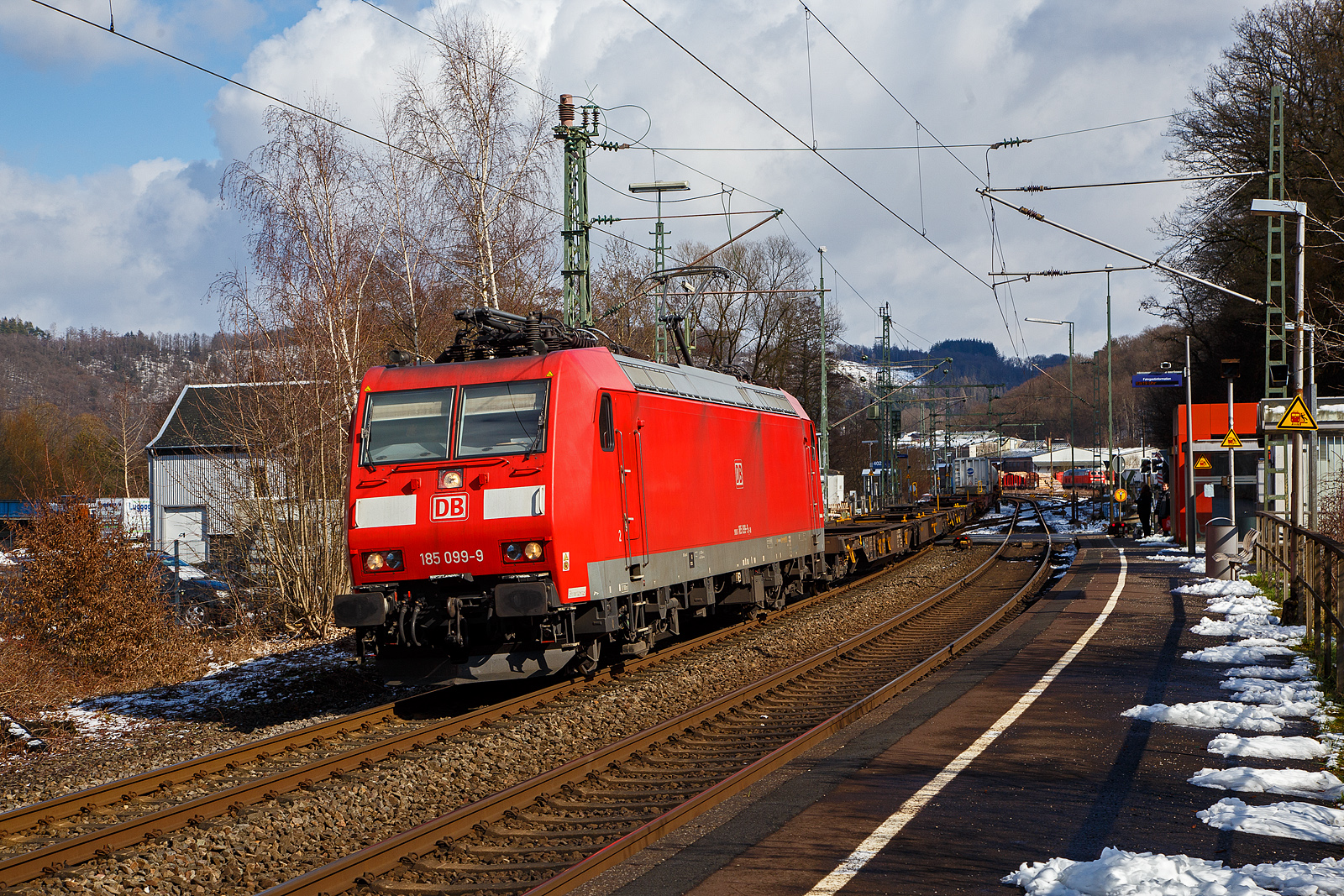 Die auch fr die Schweiz zugelassene 185 099-9 (91 80 6185 099-9 D-DB) der DB Cargo AG fhrt am 15.03.2023, mit einem KLV-Zug auf der Siegstrecke (KBS 460) durch Scheuerfeld (Sieg) in Richtung Kln.

Die TRAXX F140 AC1 wurde 2002 von der Bombardier in Kassel unter der Fabriknummer 33521 gebaut. Sie hat die Zulassung fr Deutschland und die Schweiz, man kann es auch an den vier DSA-200 Einholm-Stromabnehmer erkennen. Auen sind jeweils die fr das Schweizernetz bestimmten Stromabnehmer mit einer 500 mm schmaleren Wippenbreite von 1.450 mm und innen die DB-Netz bestimmten mit einer Wippenbreite von 1.950 mm.
