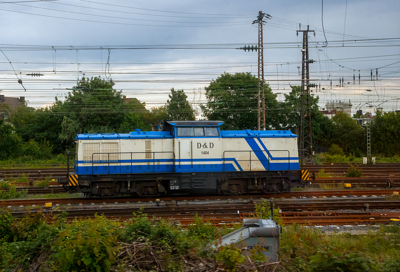 Die D&D 1404 bzw. 203 221-7 (92 80 1203 221-7 D-DUD) der D&D Eisenbahngesellschaft mbH (Hagenow), ex DB 202 735-7, ex DR 112 735-6, ex DR 110 736-8, steht am 31.05.2022 beim Bahnhof Hamm (Westf.). Aufnahme aus dem Zug heraus.

Die Diesellok eine DR V 100.1 wurde 1973 von LEW (VEB Lokomotivbau Elektrotechnische Werke „Hans Beimler“, Hennigsdorf) unter der Fabriknummer 14436 gebaut und als DR 110 735-8 an die Deutsche Reichsbahn ausgeliefert. 1986 erfolgte bereits eine Remotorisierung/Umbau im Bw Dresden und die Umzeichnung in DR 112 735-6. Zum 01.01.1992 erfolgte die Umzeichnung in DR 202 735-8 und zum 01.01.1994 dann DB AG. Die Ausmusterung bei der DB erfolgte 2001und sie ging sie die SFZ - Schienenfahrzeugzentrum (später ALS) Stendal. Von der ALS - ALSTOM Lokomotiven Service GmbH in Stendal erfolgte dann der Umbau (teilmodernisiert) in die heutige 203 221-7. Im Jahr  2006 wurde sie an die D&D Eisenbahngesellschaft mbH (Hagenow) verkauft und hat seit 2007 die UIC-Nummer 92 80 1203 221-7 D-DUD. 

TECHNISCHE DATEN:
Spurweite: 1.435 mm (Normalspur)
Achsanordnung: B'B'
Länge über Puffer: 14.240mm
Radsatzabstand im Drehgestell: 2.300mm
Drehzapfenabstand: 7.000mm
Höhe über SO: 4.255mm
Dienstgewicht: 68 t

Motor: 12-Zylinder CATERPILLAR-Dieselmotor mit Direkteinspritzung, Abgasturbolader und Ladeluftkühlung, vom Typ CAT 3512 DI-TA
Motorleistung: 1.082 kW (1.472 PS)
Nenndrehzahl: 1.800 U/min
Hubraum: 51,8 Liter (Bohrung-Ø 170 x Hub 190 mm)
Motorgewicht: 6.537 kg

Getriebe: Voith Strömungsgetriebe GSR 30/5,7
Leistungsübertragung: dieselhydraulisch
Anfahrzugkraft: 207 kN
Höchstgeschwindigkeit: 100 km/h
Kleinste Dauerfahrgeschwindigkeit: 11,1 km/h
Kleinster befahrbarer Gleisbogenradius: 80m
