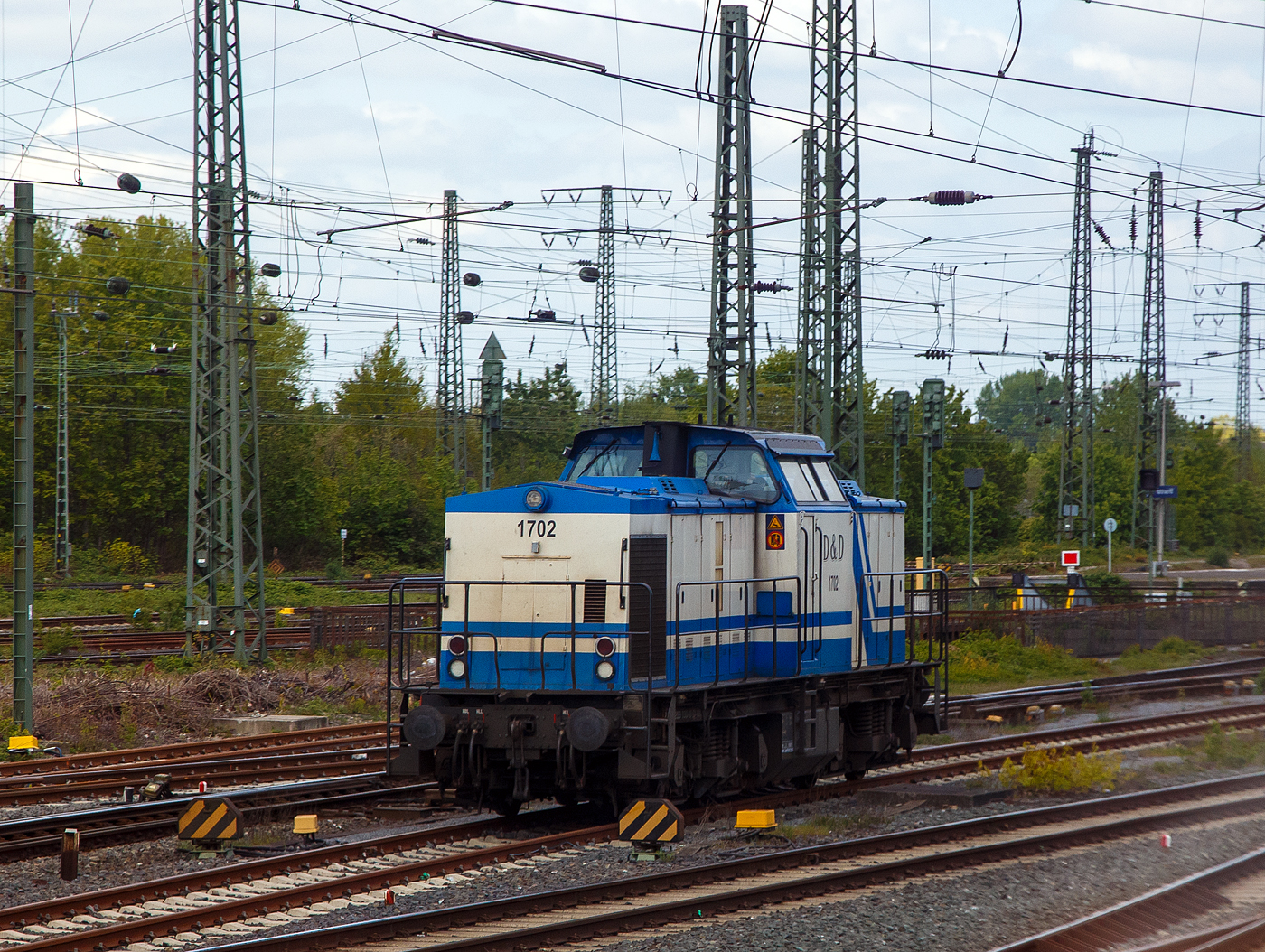 Die D&D 1702 bzw. 203 130-0 (92 80 1203 130-0 D-DUD) der D&D Eisenbahngesellschaft mbH (Hagenow), ex DB 202 602-9, ex DR 112 602-8, ex DR 110 602-0, steht am 30.04.2022 beim Bahnhof Hamm (Westf.). Aufnahme aus dem Zug heraus.

Die Diesellok eine DR V 100.1 wurde 1973 von LEW (VEB Lokomotivbau Elektrotechnische Werke „Hans Beimler“, Hennigsdorf) unter der Fabriknummer 13920 gebaut und als DR 110 602-0 an die Deutsche Reichsbahn ausgeliefert. 1984 erfolgte bereits eine Remotorisierung/Umbau im Bw Meiningen und die Umzeichnung in DR 112 602-8. Zum 01.01.1992 erfolgte die Umzeichnung in DR 202 602-9 und zum 01.01.1994 dann DB AG. Die Ausmusterung bei der DB erfolgte 1999. Im Jahre 1998 ging sie an die SFZ - Schienenfahrzeugzentrum Stendal. Von der ALS - ALSTOM Lokomotiven Service GmbH in Stendal erfolgte dann 2002 der Umbau gemäß Umbaukonzept  BR 203.1  in die heutige 203 130-0. Im Jahr  2007 wurde sie an die D&D Eisenbahngesellschaft mbH (Hagenow) verkauft.