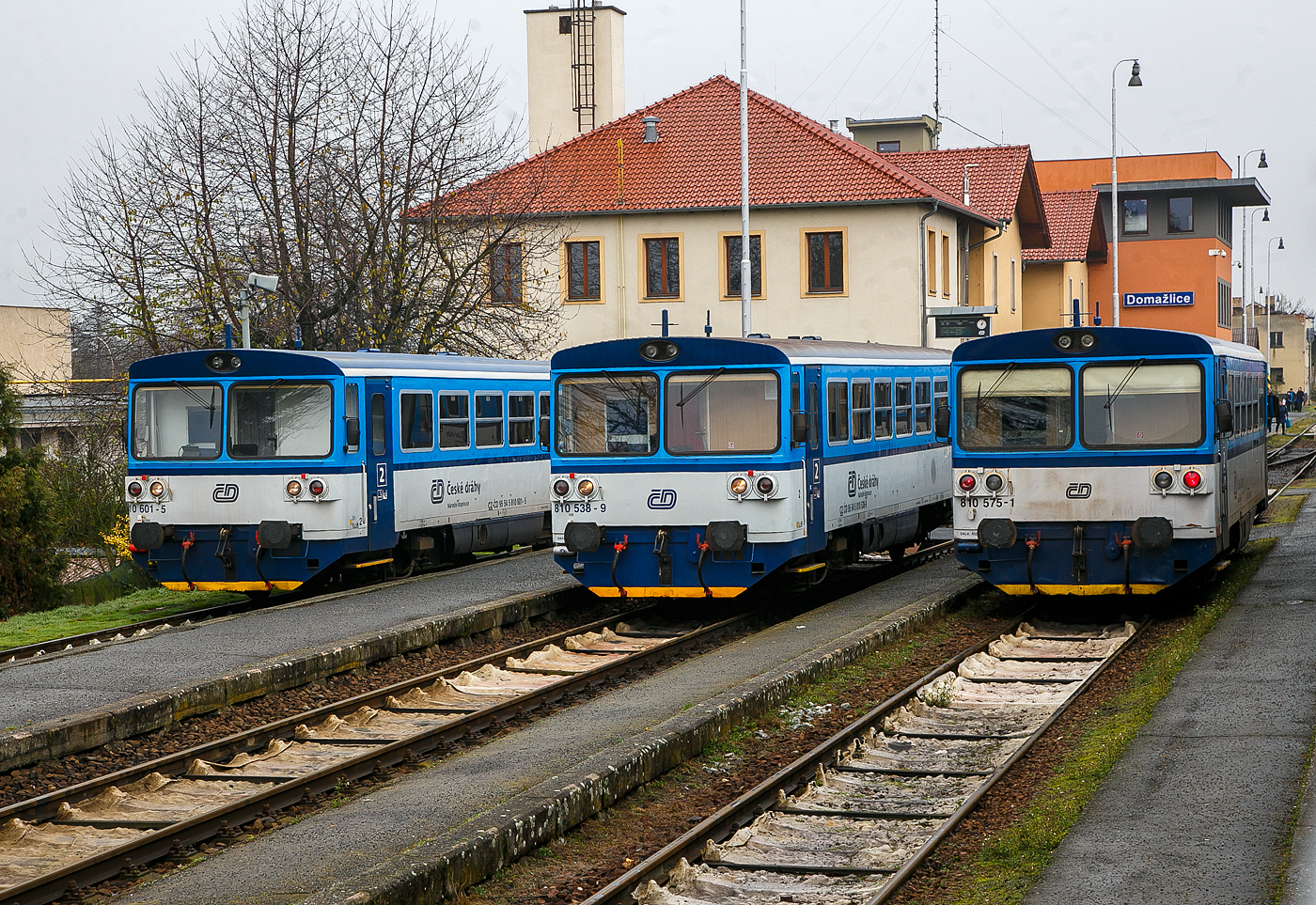Gleich drei Brotbchsen...
Die drei zur „RegioMouse“ modernisierte “Chcpk”  (Brotbchsen), zweiachsige Dieseltriebwagen der ČD BR 810 (ex ČSD M 152.0) stehen am 22.11.2022 im Bahnhof Domalice (Taus) zur Abfahrt bereit. Es sind von links nach rechts, der (CZ-ČD 95 54 5) 810 601-5, 810 538-9 und 810 575-1. 

Die zweiachsige Dieseltriebwagen fr den Regionalverkehr wurden als Baureihen M 152.0 (ab 1988: Baureihe 810) fr die Tschechoslowakischen Staatsbahnen (ČSD) gebaut. Die Fahrzeuge bilden die dritte Generation zweiachsiger Triebwagen der ČSD. Die seit 2018 einer zweiten Modernisierung unterzogenen Fahrzeuge der ČD-Baureihen 809 und 810 werden als „RegioMouse“ vermarktet.

Ab 1975 wurden bei Vagonka Tatra in Studnka (heute koda Vagonka a.s.) in sieben Bauserien 680 zweiachsige Dieseltriebwagen fr die ČSD als Baureihe M 152.0 gebaut. Nahezu baugleiche Fahrzeuge wurden an die Ungarischen Staatsbahnen (MV), als Bzmot, geliefert. Passend zu den Triebwagen wurden entsprechende Beiwagen vom Typ Blm geliefert, welche in Aufbau und Aussehen identisch mit den Triebwagen sind. Jedem Triebwagen konnten zwei Beiwagen beigegeben werden. Aufgrund der eckigen Aufbauten erhielten die Triebwagen von deutschen Eisenbahnfreunden den Spitznamen „Brotbchse“.

Zwischen 1987 und 1990 fhrten die ČSD EDV-gerechte Triebfahrzeugnummern ein. In der bergangszeit wurden die EDV-Nummern zustzlich zu den alten Gussschildern mit Klebeziffern angebracht. Die Triebwagen erhielten die Reihenbezeichnung 810, die Beiwagen 010. Beide Nachfolgeunternehmen der ČSD behielten den Nummernplan bei, allerdings wurden freizgig einsetzbare Beiwagen 2009 auch nummernmig in den Reisezugwagenpark aufgenommen.

Nach der Teilung der Tschechoslowakei in die Nachfolgestaaten Tschechien und Slowakei am 1. Januar 1993 wurden Trieb- und Beiwagen auf die neugegrndeten Staatsbahnen ČD und SR aufgeteilt. In der Slowakei gehren die Fahrzeuge heute zum Bestand des Nachfolgeunternehmens elezničn spoločnosť Slovensko (ZSSK).

Technische Merkmale:
Die Triebwagen haben keine Vielfachsteuerung, passende Steuerwagen existieren nicht. Deshalb muss bei mehrteiligen Einheiten jeder Triebwagen mit einem Triebfahrzeugfhrer besetzt sein. Die Triebwagen mssen, wenn sie mit entsprechenden Beiwagen verkehren,  an Endbahnhfen stets an die jeweilige Zugspitze umgesetzt werden.

Aufbau des Triebwagens:
Der Triebwagen ist eine Leichtbaukonstruktion. Der Wagenkasten besteht aus gewalzten und abgekanteten Stahlprofilen, die mit Stahlblech verkleidet sind. Innen ist das Gerippe mit Spanplatten, die mit Sprelacart berzogen sind, verkleidet. Der Fuboden besteht aus wasserbestndigem Sperrholz von 15 Millimetern Dicke und ist mit einer zwei Millimeter starken Schicht aus PVC beklebt. An jedem Ende des Wagenkastens befindet sich ein vom Fhrerstand abgetrennter Einstiegsraum, der auf beiden Seiten jeweils eine vom Fhrerstand schliebare pneumatische Schiebetr besitzt.

Das Fahrgastabteil besitzt 56 Sitzpltze in der Anordnung 3+2 mit Mittelgang, die ursprnglich schaumgummigepolstert waren. Zustzlich bietet ein Wagen etwa 40 Stehpltze. Der Fahrgastraum hat auf jeder Seite sechs Fenster mit der lichten Weite von 1316  841 mm, deren oberer Teil klappbar ist. Groe Frontscheiben mit Scheibenheizung, Scheibenwischern und Sonnenschutzblende ermglichen eine gute Streckenbeobachtung. Durch die Anordnung einer zustzlichen Trennwand fielen die Fhrerstnde sehr kurz aus. Um eine befriedigende Sitzposition fr den Triebwagenfhrer zu ermglichen, musste die Trennwand im Bereich seines Sitzes ausgeschnitten werden. Der Ausschnitt ist mit einer in den Einstiegsraum reichenden Blechabdeckung verschlossen.

Die Beiwagen entsprechen im Aufbau den Triebwagen, abgesehen von der fehlenden Antriebsanlage. An Stelle der Fhrerstnde ist an den Wagenenden eine durchgehende Sitzbank vorhanden.

Laufwerk und Antriebsanlage:
Gefhrt wird das Fahrzeug von zwei einachsigen Drehgestellen, von denen eines ber eine Gelenkwelle angetrieben wird. Damit sind beide Radstze im Bogen radial einstellbar. Die Drehgestelle sttzen sich mit Schraubenfeder auf den Achslagern ab. Die Aufhngungen sind mit dem Wagenkasten ber Gummiblcke verbunden. Auf der Treibachse, die beidseitig gesandet werden kann, sitzt das Wendegetriebe zur Umsteuerung der Fahrtrichtung. Bei den Triebwagen sind beide Radstze mit einer Spurkranzschmiereinrichtung ausgerstet.

Als Antriebsanlage ist ein nicht aufgeladener Dieselmotor vom Typ LIAZ ML 634 unterflur eingebaut. Dieser besitzt sechs Zylinder in Reihe mit Direkteinspritzung und ist mit dem Getriebe vom Typ Praga 2M 70 direkt verbunden. Die gesamte Antriebsanlage besteht bis auf das Achswendegetriebe aus Komponenten, die vom Omnibus Karosa M 11 bernommen wurden. 

Die Antriebsanlage und die Hilfseinrichtungen wie Wasserkhlung, lwrmetauscher, Batterie, Kraftstoffbehlter und Warmwasserheizung sind unterflur angeordnet. Deshalb drfen die Triebwagen Ablaufberge nicht befahren. Die Hilfsmaschinen, ein Wechselstromgenerator und ein Kompressor fr die Druckluft der pneumatischen Bremse, werden ber Gelenkwelle und Keilriemen vom Dieselmotor angetrieben. Der Dieselmotor ist wassergekhlt, zustzlich ist ein Lfter mit hydrostatischem Antrieb vorhanden. Dieser wird in Abhngigkeit von der Motordrehzahl und der Khlwassertemperatur automatisch geregelt.

brige Einrichtungen:
Die Triebwagen sind mit indirekter Bremse und direkter Bremse nach dem System DAKO ausgerstet. Gesteuert wird diese mit dem Fhrerbremsventil koda N – 0. Auerdem ist eine Handbremse, die in beiden Fhrerstnden bedient werden kann, vorhanden. In beiden Einstiegsrumen und dem Fahrgastraum befinden sich Notbremshhne.

Beheizt wird das Fahrgastabteil des Triebwagens durch Warmluft. Hierzu wird das Khlwasser aus dem Motorkreislauf einem Wrmetauscher zugefhrt, der unter den Sitzen angebracht ist. Bei nichtarbeitendem Dieselmotor wird ein Vorwrmgert verwendet. Der Fhrerstand wird mit einer Warmwasserheizung beheizt. Die Beiwagen werden elektrisch beheizt. Belftet wird das Abteil der Reisenden ber Dachlfter. Die Beleuchtung des Fahrgastabteiles bernimmt der Wechselstromgenerator. Durch die Ausrstung der Trieb- und Beiwagen mit Seitenpuffern und Schraubenkupplung ist es mglich, die Fahrzeuge mit anderen Fahrzeugen zu kuppeln. Daher knnen die Triebwagen vereinzelte Gtertransporte auf Nebenbahnen durchfhren. Die Schraubenkupplungen entsprechen der bei Dieseltriebwagen der ČSD blichen leichten Ausfhrung, die damit ausgersteten Wagen drfen in Regelzgen nur am Schluss eingestellt werden.

Umbauten in Tschechien  (der ČD): 
1994 begann der Umbau von 28 Einheiten fr den schaffnerlosen Betrieb. Dabei wurde die Inneneinrichtung gendert. 1996 wurden diese Einheiten in die ČD-Baureihe 809 umgezeichnet.

Von 2005 bis 2012 wurden die Fahrzeuge der ČD durch die Firma Pars Nova (gehrt zu koda) grundlegend modernisiert und umgebaut. Dabei entstanden zweiteilige Einheiten, die jeweils aus einem Triebwagen und einem teilweise niederflurigen Steuerwagen bestehen. Ein Teil der Triebzge wurde als dreiteilige Einheit mit zwei Triebwagen und einem dazwischen eingestellten Beiwagen zusammengestellt. Bei den Wagen, die einen zwischen den Radstzen abgesenkten Wagenboden erhielten, wurden die Einstiege von den Enden in Wagenmitte verlegt.

Im Februar 2018 wurde als letzte Modernisierung die Baureihe 816 von GW Train Regio vorgestellt.

Einsatz:
Die Fahrzeuge besitzen eine Zulassung fr den Verkehr nach Deutschland und sterreich. Im grenzberschreitenden Nahverkehr gehrten sie auf den Grenzbahnhfen Zittau, Ebersbach (Sachs), Bad Schandau, Johanngeorgenstadt, Furth im Wald und Bayerisch Eisenstein zum tglichen Bild. 

Trotz des Umbauprogrammes existieren nach wie vor einige Fahrzeuge, die sich bis auf eine Teilmodernisierung des Fahrgastraumes mit neuer Bestuhlung noch weitgehend im Originalzustand befinden. Sie kommen weiterhin auf Strecken mit geringem Verkehrsaufkommen planmig zum Einsatz. Bei den ČSD war es blich, Beiwagen von Verbrennungsmotortriebwagen auch als lokbespannte Reisezge einzusetzen. Die Nachfolger behielten diese Betriebsweise bei.

TECHNISCHE DATEN :
Hersteller: ČKD Vagnka in Studnka (heute koda Vagonka a.s.)
Spurweite: 1.435 mm (Normalspur)
Achsformel: 1'A' 
Lnge ber Puffer: 13.970 mm
Hhe: 3.500 mm
Achsabstand: 8.000 mm
Dienstgewicht: 20 t
Radsatzfahrmasse: 10 t
Hchstgeschwindigkeit: 80 km/h
Installierte Leistung: 155 kW (bei 1.950 U/min)
Anfahrzugkraft: 29 kN 
Motorbauart: Sechszylinder-Reihendieselunterflurmotor
Motorentyp: LIAZ ML 634
Motorhubraum: 11,946 Liter (Zylinder- 130 mm / Kolbenhub 150 mm)
Nenndrehzahl: 2.150 U/min (Leerlaufdrehzahl 600 U/min)
Kompressionsverhltnis: 12,5 : 1
Getriebe: Praga 2M70
Leistungsbertragung: hydromechanisch
Sitzpltze: 55
Tankinhalt: 300 l
Fubodenhhe: 570 mm (Niederflurteil)
Kleinster befahrbarer Gleisbogen: R 100 m

Quellen: Wikipedia, atlaslokomotiv.net
