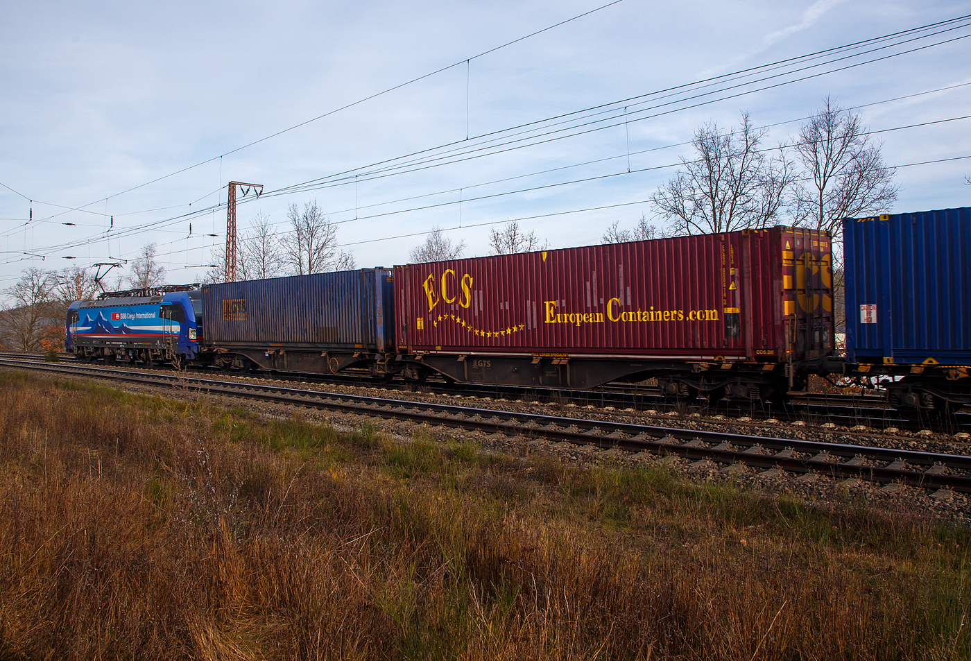 Hinter der an die SBB Cargo International AG vermietete SIEMENS Vectron MS 193 530  Po , der sechsachsige Drehgestell-Gelenk-Containertragwagen-Einheit (6-achsiger Containertragwagen), 3 54 4962 273-7 CZ-GTSL der Gattung Sggmrss, der italienischen GTS Logistic (Bari), am 22.02.2023 im Zugverband bei der Zugdurchfahrt in Wilnsdorf-Rudersdorf (Kr. Siegen), hier beladen mit zwei Containern.

TECHNISCHE DATEN:
Spurweite: 1.435 mm
Anzahl der Achsen: 6 in drei Drehgestellen
Länge über Puffer: 29.590 mm
Drehzapfenabstand: 2 x 11.995 mm
Achsabstand im Drehgestell: 1.800mm
Laufraddurchmesser: 920 mm (neu)
Ladelänge : 2 x 13.820mm (2 x 45 ft)
Höhe der Ladeebene über SOK: 1.155 mm
Eigengewicht: ca. 28.000 kg
Max. Zuladung bei Lastgrenze S: 107,0 t (ab Streckenklasse D)
Max. Zuladung bei Lastgrenze SS: 92,0 t (ab Streckenklasse C)
Max. Geschwindigkeit: 100 km/h (Lastgrenze SS oder leer 120 km/h)
Kleinster bef. Gleisbogenradius: R 75 m
Verwendungsfähigkeit: TEN-GE