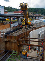 Hering Bau/897067/nun-im-einsatz-der-125-t Nun im Einsatz der 125 t KIROW Gleisbauschienenkran KIROW Multi Tasker KRC 810 T (mit Schwerlastausrüstung), Schweres Nebenfahrzeug Nr. D-HGUI 99 80 9419 024-1, ex 97 82 53 513 19-3, der HERING Bahnbau GmbH (Burbach) ist am 29 September 2025 im Betzdorf/Sieg. 

Hier im Bereich unter dem P+R Parkhaus bis zum Fluss Sieg werden Horizontalbohrungen gemacht, vermutlich für erforderliche Entwässerungs-Leitungen. So mussten Bohrrohre in die Baugrube gehoben werden und wie hier der Abraum aus der Baugrube gehoben werden. Eigentlich ist ein 125 t Kran damit unterfordert (überdimensioniert), aber man muss bedenken es wurde eine weite Auskragung (Ausladung vor Puffer) und das freistehend (Nichtabgestützt) benötigt. 

Der hier mit der Ausladung vor Puffer von über 15 m könnte der Kran freistehend 30 t heben, aber darf dann nicht schwenken. Wenn geschenkt werden muss liegt diese dann nur bei 1,5 t. Entscheidend für die Ausladung des Auslegers ist aber auch die hintere Ausladung des Gegengewichts. 