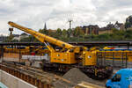 Hering Bau/897072/nun-im-einsatz-der-125-t Nun im Einsatz der 125 t KIROW Gleisbauschienenkran KIROW Multi Tasker KRC 810 T (mit Schwerlastausrüstung), Schweres Nebenfahrzeug Nr. D-HGUI 99 80 9419 024-1, ex 97 82 53 513 19-3, der HERING Bahnbau GmbH (Burbach) ist am 29 September 2025 im Betzdorf/Sieg. 

Hier im Bereich unter dem P+R Parkhaus bis zum Fluss Sieg werden Horizontalbohrungen gemacht, vermutlich für erforderliche Entwässerungs-Leitungen. So mussten Bohrrohre in die Baugrube gehoben werden und wie hier der Abraum aus der Baugrube gehoben werden. Eigentlich ist ein 125 t Kran damit unterfordert (überdimensioniert), aber man muss bedenken es wurde eine weite Auskragung (Ausladung vor Puffer) und das freistehend (Nichtabgestützt) benötigt. 

Der hier mit der Ausladung vor Puffer von über 15 m könnte der Kran freistehend 30 t heben, aber darf dann nicht schwenken. Wenn geschenkt werden muss liegt diese dann nur bei 1,5 t. Entscheidend für die Ausladung des Auslegers ist aber auch die hintere Ausladung des Gegengewichts. 

Der Kran wurde 2008 von KIROW in Leipzig unter der Fabriknummer 149000 gebaut und an die HERING Bahnbau GmbH (Burbach) geliefert.

Der Gleisbauschienenkran KRC 810 T ist ein Schienendrehkran des Herstellers Kirow Ardelt (bis 2008 Kirow) in Leipzig. Der Typ 810 wird für den Aus-und Einbau von schweren Betonweichen, Gleisjochen und Hilfsbrücken sowie für die Montage von Ingenieurbauwerken eingesetzt. Bei Havarien auf Bahnstrecken leistet er schnelle Hilfe zum Bergen schwerer Lasten. Das maximale Lastmoment des Krans liegt zwischen 500 und 900 tm. Die Krane werden auch als Eisenbahndrehkran „EDK“ bezeichnet.

Die maximale Tragfähigkeit des bis zu 128 Tonnen schweren Krans beträgt abgestützt bis zu 125 Tonnen und freistehend 90 Tonnen. Bei maximaler Ausladung kann der Kran noch 28,5 Tonnen heben. Die größte mögliche Hakenhöhe liegt bei 18 m und die maximale Ausladung vor Puffer bei 15 m. Der Teleskoparm erlaubt Arbeiten im Radius zwischen 6,5 und 24,5 Metern. Im Gegensatz zu früheren Kranen ist auch ein Einsatz in der Nullposition ohne Abbau der Fahrleitung möglich. Die Gegenlast (Gegengewicht) ist zum Ausgleich unterschiedlicher Lasten ausfahrbar. Die Gegenlast kann in Transportstellung nicht (wie z.B. bei dem KRC 910) auf einem Gegenlastwagen abgestützt werden. Dadurch hat KRC 810 auch eine höhere Streckenlast (als z.B. der KRC 910). Für Hebearbeiten instehender Stellung verfügt der Kran über hydraulisch-ausfahrbare Stützen. Die Höchstgeschwindigkeit 19 km/h mit dem Eigenantrieb und 120 km/h im Zugverband geschleppt.  Zu dem Kran gehören zwei Kranschutzwagen. Die zulässige Anhängelast beträgt 80 t.

TECHNISCHE DATEN:
Spurweite: 1.435 mm (Normalspur)
Anzahl der Achsen: 8
Achsfolge: [(1A)(1A)][(A1)(A1)]
Länge über Puffer: 13.000 mm (ohne Ausleger)
Drehzapfenabstand: 8.000 mm
Drehzapfenabstand im Drehgestell 1 und 2: 2.300 mm
Achsabstand in den Einzeldrehgestellen: 1.100 mm
Ergebene Achsabstände in m: 1,1 / 1,2 / 1,1/ 4,6 / 1,1 / 1,2 / 1,1
Treib- und Laufraddurchmesser: 730 mm (neu) / 680 mm (abgenutzt)
Höhe in Transportstellung: 4.250 mm
Breite in Transportstellung: 3.100 mm
Eigengewicht: 128 t
Dieselmotor: Wassergekühlter 6-Zylinder Reihenmotor mit Abgasturboaufladung und Ladeluftkühlung vom Typ Cummins M 11 – C 315
Motorleistung: 235 kW bei 1.800 U/min
Max. Drehmoment: 1.458 Nm bei 1.300 U/min
Not-Dieselmotor: Luftgekühlter 2-Zylinder Viertakt-Dieselmotor mit Direkt-Einspritzung vom Typ Hatz 2 G 40 mit einer Leistung11,5 kW bei 2.300 U/min.
Fahrgeschwindigkeit im Zugverband: 120 km/h (geschleppt)
Fahrgeschwindigkeit mit Eigenantrieb: 20 km/h
zul. Anhängelast: 80 t
Hakenhöhe (max.): 18 m
Ausladung (max. vor Puffer): 16 m
Zugelassen als Schwerwagen für Streckenklasse: CS 05
Maximale Radsatzlast: 16 t
Streckenlast (Meterlast):  9,9 t/m
kleinster befahrbarer Radius: 00 m
Bremse: KE-GP-D- m.Z. (Scheibenbremsen auf allen Rädern)
Sekundär Scheibenbremsen auf allen Rädern
Handbremse: hydro-mechanisch auf alle Radsätze
Kraftstoffvorrat: 990 l

Tragfähigkeiten:
bei 0,00 m Ausladung vor Puffer, mit Schwerlastausrüstung: 125 t
bei 2,80 m Ausladung vor Puffer, ± 30°, abgestützt: 90 t
bei 2,80 m Ausladung vor Puffer, ± 20°, freistehend: 46 t