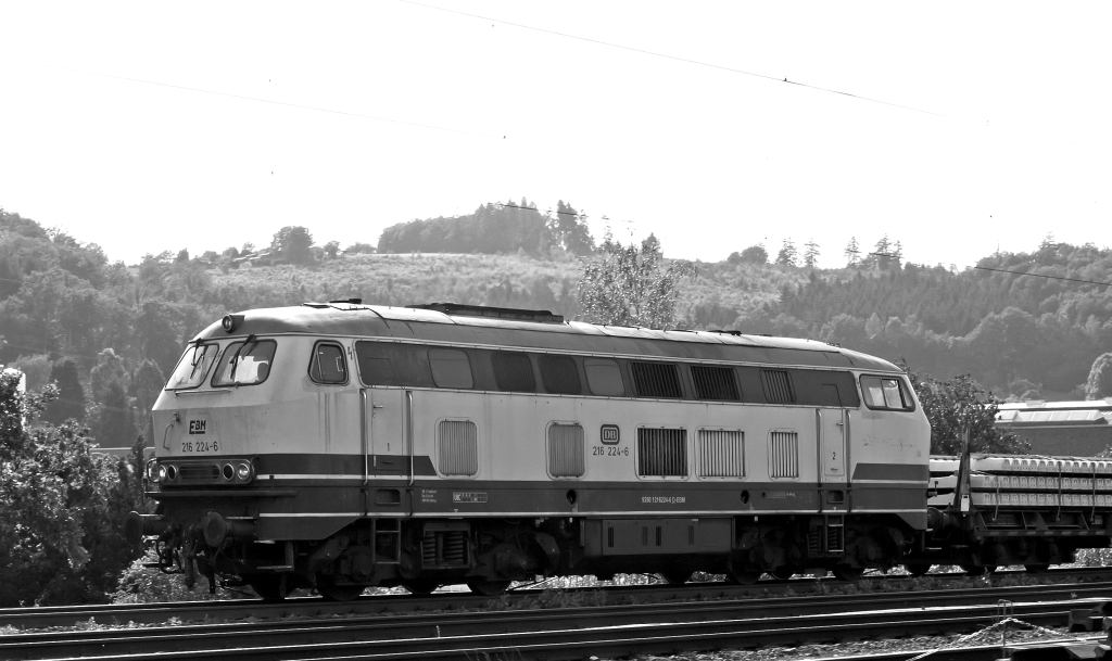 Die 216 224-6 der EBM Cargo (Gummersbach) kommt mit einem Schwellenzug am 29.07.2011  in Siegen (Kaan-Marienborn) und fhrt Richtung Wilnsdorf-Rudersdorf . Die Lok wurde 1968 bei Krupp unter der Fabriknummer 4885 gebaut, es war die letzte der Serie.
Hier im Gegenlicht.