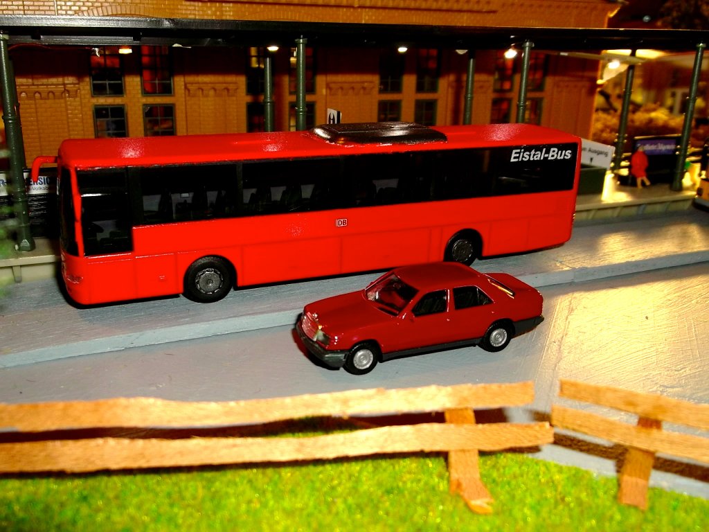 Ein selbst lackierter Mercedes-Benz Integro II (Hersteller AWM) steht am Bahnhof meiner Modelleisenbahnanlage. Der Modellbus wurde von mir in der Original-Farbe  verkehrsrot  (RAL 3020) lackiert und mit dem DB-Logo sowie dem Schriftzug  Eistal-Bus  versehen.  Eistal-Bus  ist die fiktive DB-Regiobus-Tochter meiner Modellwelt.
Im Vordergrund befindet sich ein - ebenfalls selbst lackierter - Mercedes Benz W124 300E.