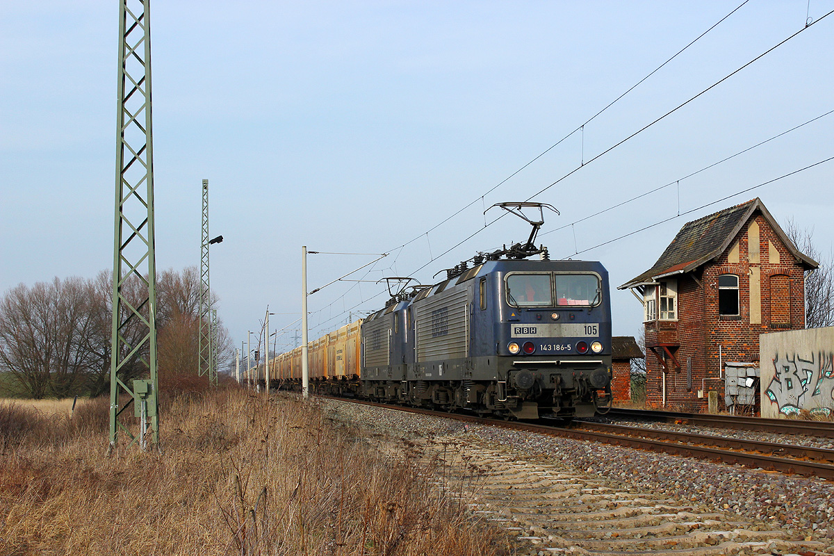 01.03.2014 - Der derzeit sehr zuverlässig und pünktlich verkehrende Holzhackschnitzelzug der RBH von Wismar nach Mannheim passiert gezogen von RBH 105 + 120 das stillgelegte nördliche Stellwerk des einstigen Bahnhofs Demker.