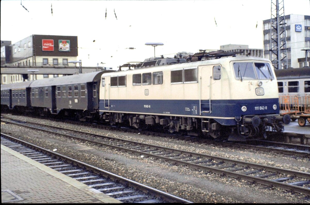 111 042-8 mit einer Garnitur Umbauwagen auf den Bayerischen Gleisen (Gleis 25 bis 28) in Ulm, nach Regensburg am 28.11.1981. (Die Strecke war zu diesem Zeitpunkt erst seit kurzer Zeitelektrifiziert).