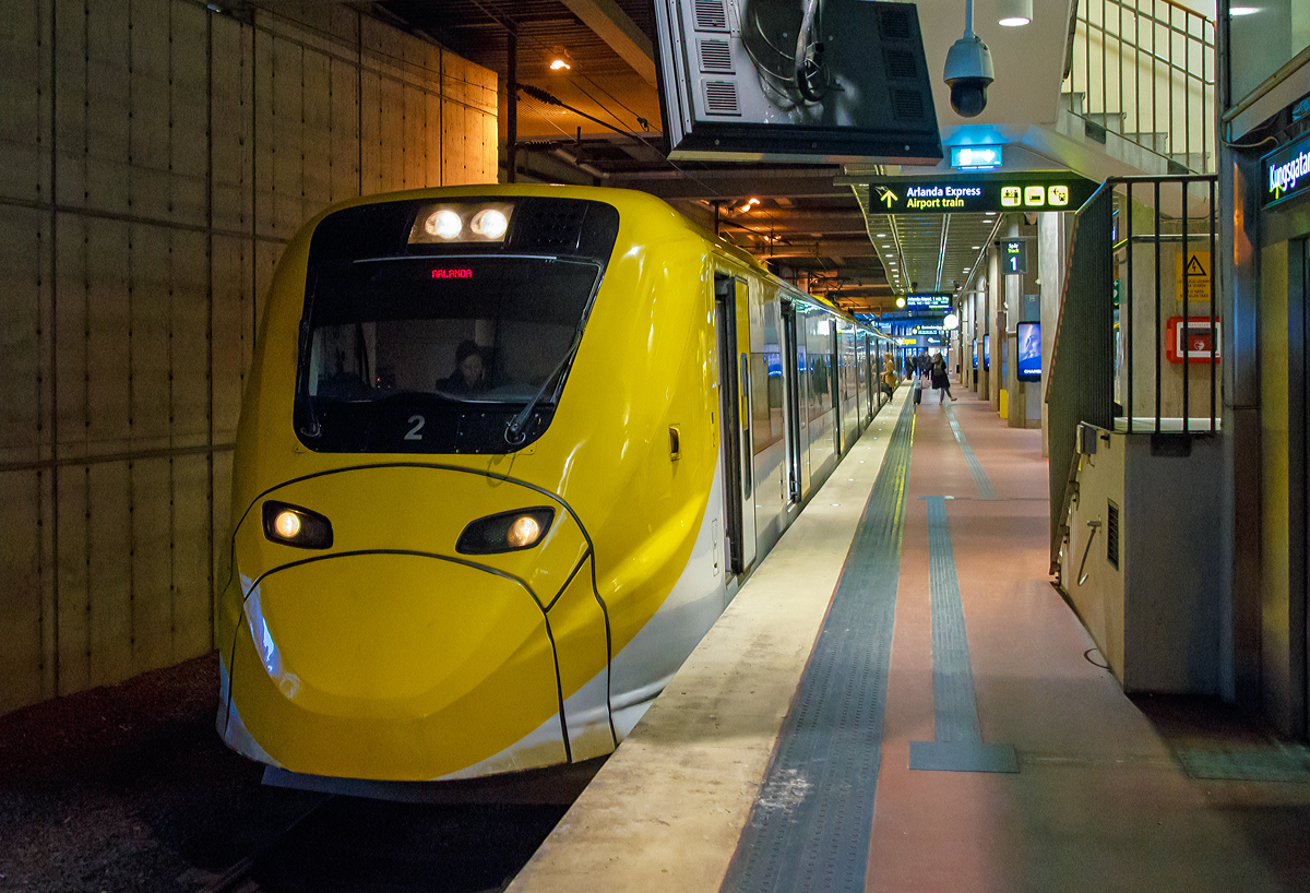 
Der Arlanda Express Triebzug 2, ein Alstom Coradia X3, steht am 21.03.2019 auf Gleis 1 in Stockholm Central zur Abfahrt nach dem Flughafen Stockholm/Arlanda bereit.

Der vierteilige, normalspurige elektrische Triebwagenzug vom Typ X3 wird von der schwedischen Gesellschaft Arlanda Express für den direkten Verkehr zwischen Stockholm C und Flughafen Stockholm/Arlanda verwendet.

Von Alstom wurden sieben dieser klimatisierten Züge in Birmingham gebaut und 1998/99 geliefert. Der X3 gehört zur Obergruppe der Coradia-Triebwagen und kann Geschwindigkeiten bis 205 km/h erreichen. Die Züge sind weiß und gelb lackiert. Die Triebwagen nutzen das gleiche Stromsystem, wie es im gesamten schwedischen Eisenbahnnetz vorhanden ist.

TECHNISCHE DATEN:
Spurweite: 1435 mm (Normalspur)
Achsformel: Bo'Bo'+2'2'+'2'2+Bo'Bo'
Länge über Kupplung: 93.084 mm
Dienstgewicht: 187 t
Höchstgeschwindigkeit: 200 km/h
Leistung: 2.240 kW
Stromsystem: 15 kV 16 2/3 Hz ~
Sitzplätze: 228

Arlanda Express ist eine schwedische Bahnverbindung, die mit dem 200 km/h schnellen Elektrotriebzug X3 seit 1999 den Stockholmer Hauptbahnhof mit dem Flughafen Stockholm/Arlanda verbindet. Die Züge bewältigen die Strecke in 20 Minuten. Am Flughafen bedienen sie die Stationen Arlanda Södra und Arlanda Norra. Die Züge verkehren bis auf wenige Ausnahmen in den Tagesrandzeiten alle 15 Minuten, im Berufsverkehr etwa alle zehn Minuten.

In Arlanda und im Hauptbahnhof von Stockholm am Gleis 1 und 2 haben die Züge gesonderte Bahnsteige. Dort ist ein direkter stufenloser Übergang vom Zug zum Bahnsteig möglich. Jeder Wagen verfügt über zwei Türen und an jeder Tür sind Gepäckablagen vorhanden. Der gesamte Zug besitzt 190 Sitzplätze. In einem der Wagen sind gesonderte Plätze für Rollstuhlfahrer sowie ein WC vorhanden.
