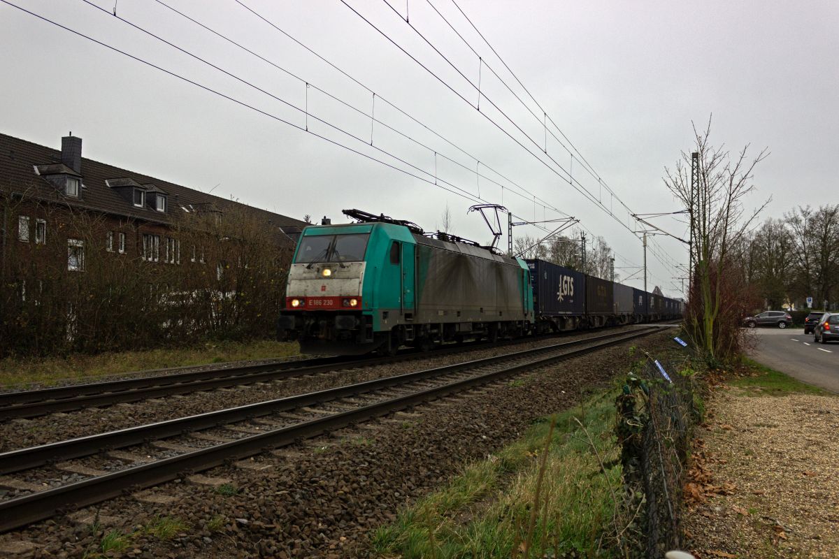 Die Bahnstrecke Neuss-Krefeld verl�uft in Meerbusch-Osterath mitten durch den Ort, wo noch zahlreiche Bahn�berg�nge vorhanden sind, die aufgrund der recht hohen Streckenbelegung teils l�ngere Schlie�zeiten aufweisen. In diesem Fall war 186 230 mit einem Containerzug der einzige Zug, sodass der Bahn�bergang im Hintergrund zwischen der Breite Stra�e und der passend benannten Stra�e An der Bundesbahn schnell wieder freigegeben wurde.