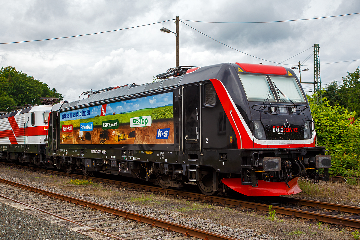 Die Bombardier TRAXX F160 AC3 LM, 187 420-5 (91 80 6187 420-5 D-EBS) der EBS - Erfurter Bahnservice GmbH steht am 05.07.2021 in Scheuerfeld (Sieg) beim Kleinbahnhof der WEBA (Westerwaldbahn), fr ihre nchste Aufgabe der Abfuhr von schweren Holzzgen, bereit.

Die Bombardier TRAXX F160 AC3 LMD wurde 2019 von Bombardier in Kassel unter der Fabriknummer 35595 gebaut. Nach meiner Sichtung hat die Lok die Zulassung fr Deutschland (D) und sterreich (A). Fr Ungarn und Rumnien sind die Zulassungen noch nicht erteilt (H und RO sind durchgestrichen).

Wie die Vorgngerinnen AC1 und AC2 ist die AC3 fr den Betrieb unter 15 Kilovolt bei 16,7 Hertz, sowie unter 25 Kilovolt bei 50 Hertz Wechselstrom ausgelegt, und verfgt unverndert ber eine Dauerleistung von 5.600 kW und eine Anfahrzugkraft von 300 kN. Von den Traxx 2E bernommen wurde der Maschinenraum mit Seitengang um das sogenannte Powerpack, bestehend aus Stromrichter und Hochspannungsgerst, womit erstmals alle Varianten dasselbe Layout verwenden.

Neu ist die Kopfform der Traxx-3-Lokomotiven, im Wesentlichen ein auf dem Lokkasten aufgesetztes GFK-Modul. Zudem wurden die Lokomotiven erstmals ab Werk konstruktiv fr den Einbau der Zugbeeinflussung ETCS vorbereitet. Neuerungen betreffen die verfgbaren Drehgestelle: zu den bisherigen Varianten „F140“ mit Tatzlagerantrieb und Zulassung fr maximal 140 km/h, und „P160“ mit Hohlwellenantrieb und Zulassung fr maximal 160 km/h, werden die Traxx-3-Lokomotiven offiziell auch als Variante „F160“ mit Tatzlagerantrieb und Zulassung fr maximal 160 km/h angeboten.

Gnzlich neu sind die optional verfgbaren Last-Mile-Module, die es als Last-Mile-Diesel (LMD) mit zustzlicher Last-Mile-Battery (LMB) gibt. Das LMD besteht aus einem Dieselhilfsmotor und einem Kraftstofftank, um auch nicht-elektrifizierte Streckenabschnitte und Anschlussgleise befahren zu knnen. Der Dieselmotor von Deutz verfgt ber einen Hubraum von 7.150 cm, erbringt eine Leistung von 230 kW (180 kW am Rad), mit Batterieuntersttzung 290 kW und erfllt die Stage-IIIB-Abgasnorm. Im Dieselbetrieb werden alle vier Fahrmotoren betrieben, die Anfahrzugkraft betrgt dabei mit Batterieuntersttzung unverndert 300 kN, ohne Batterie 260 kN. Ohne Anhngelast ist damit eine Hchstgeschwindigkeit von 60 km/h mglich, bei 2000 Tonnen Last noch 40 km/h. Der Tankinhalt von 400 Litern reicht fr bis zu acht Stunden Dieselbetrieb, kurze Strecken knnen auch ausschlielich mit der eingebauten Batterie zurckgelegt werden. Der bergang vom elektrischen zum Dieselbetrieb kann whrend der Fahrt erfolgen. Fr den Rangierbetrieb ist zudem eine Funkfernsteuerung erhltlich.

Erstmals wurde der Lokkasten nicht mit glatten Seitenwnden gefertigt, sondern konstruktiv deutlich gnstiger, sind die Seitenwnde der AC3 vertikal gesickt und die Seitenflchen erhielten sogenannte Flex-Panels, eine Vorrichtung zum Einspannen von Planen. Diese wrden die Sicken verdecken, und wren kostengnstiger als Umlackierungen oder Umbeklebungen. Die Nutzung der Flex-Panels wurde jedoch in der Schweiz umgehend untersagt.

TECHNISHE DATEN:
Hersteller:  Bombardier Transportation
Spurweite:  1.435 mm (Normalspur)
Achsanordnung: Bo’ Bo’
Lnge ber Puffer: 18.900 mm
Drehzapfenabstand: 10.440 mm
Achsabstand im Drehgestell: 2.600 mm
Treibraddurchmesser:  1.250 mm (neu) / 1.170 mm (abgenutzt)
Hhe:  4.283 mm
Breite:  2.977 mm
Lichtraumprofil: UIC 505-1
Dienstgewicht:  87 t
Fahrmotoren: 4 Asynchronmotoren
Bremse: Elektrische Bremse (SW-GPR-E mZ)

Daten im Oberleitungsbetrieb:
Hchstgeschwindigkeit: 160 km/h
Dauerleistung: 5.600 kW 
Kurzzeitleistung  Power Boost : 6.000 kW
Anfahrzugkraft: 300 kN
Dauerzugkraft: 252 kN bei 80 km/h
Stromsystem:  15 kV 16,7 Hz~ und 25 kV 50 Hz~

Daten im Dieselbetrieb (Last-Mile):
Nenndrehzahl: 1.800 U/min
Hchstgeschwindigkeit:  60 km/h
Dauerleistung: 230 kW (180 kW am Rad),
Tankinhalt:  400 l