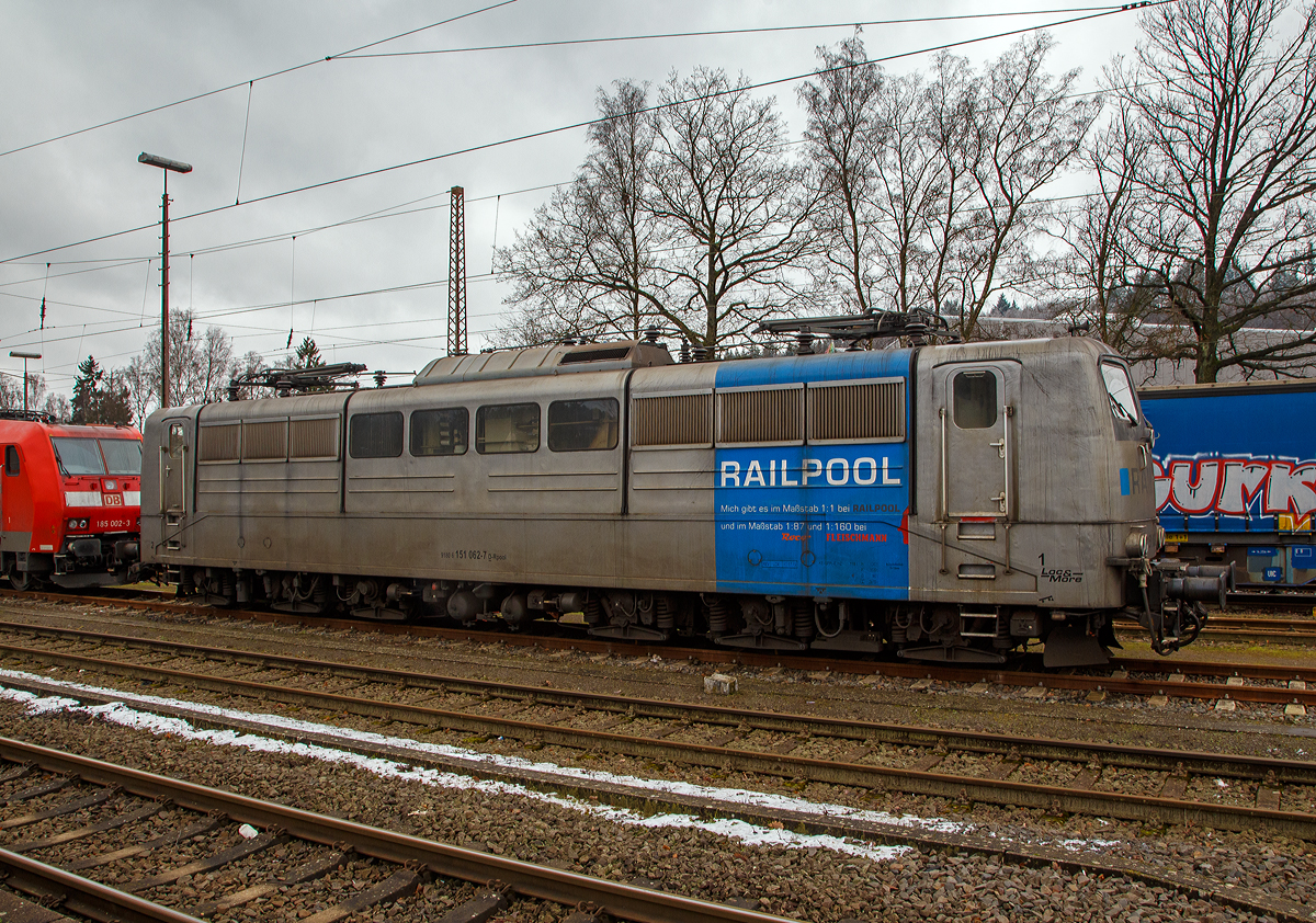 Die DB Cargo AG vermietete Railpool 151 062-7 (91 80 6151 062-7 D-Rpool) steht am 08.012022 in Kreuztal in der Abstellgruppe. 

Die Lok wurde 1974 von Henschel & Sohn in Kassel unter der Fabriknummer 31805 gebaut und an die Deutsche Bundesbahn geliefert. Bis 31.12.2016 gehörte sie zur DB Cargo AG. Zum 01.01.2017 wurden je 100 sechsachsige elektrische Altbau-Lokomotiven der Baureihen 151 und 155 an ein Konsortium aus dem Lokvermieter Railpool verkauft. Die DB Cargo mietet daraufhin 100 Loks von Railpool wieder an. Die anderen Maschinen werden dem freien Markt angeboten.

Wie auch die Werbung auf  ihr zeigt: Die Lok gibt es im Maßstab 1:1 bei RAILPOOL und im Maßstab 1:87 bei Roco und im Maßstab 1:160 bei Fleischmann. Wobei mir persönlich gefällt sie in der Farbgebung nicht gerade. Zudem könnte sie mal eine Wäsche vertragen.
