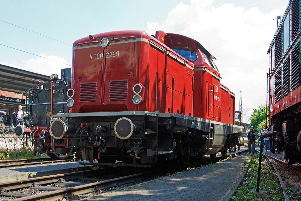 
Die Die V100 2299 (92 80 1212 229-9 D-VEB), ex DB 212 299-2, der VEB (Vulkan-Eifel-Bahn) ist am 31.05.2014 im DGEG Eisenbahnmuseum Neustadt/Weinstraße (Pfalzbahn - Museum), beim Dampfspektakel 2014, abgestellt. 
Die V 100.20 wurde 1965 bei MaK unter der Fabriknummer 1000346 als V 100 2299 für die DB gebaut. 1968 wurde sie 212 299-2 umbezeichnet, die Ausmusterung bei der DB erfolgte 2002., über ALS, Stendal ging sie dann an die VEB die sie wieder in V 100 2299 um bezeichnete, wobei sie die NVR-Nummer 92 80 1212 299-2 D-VEB trägt. Die Leistung der Lok beträgt 993 kW / 1.350 PS, die Höchstgeschwindigkeit 100 km/h.

Nachdem man eine der Vorserienloks der V100.10 probeweise mit einem 1350 PS starken Motor versehen hatte und diese sich im Betrieb bewährte, wurde zunächst eine Serie von 20 Lokomotiven bestellt, die bis auf den stärkeren Motor der Serie der V100.10 entsprachen.
Bei der ab 1963 gelieferten Serien wurde dann der Rahmen um 200 mm verlängert und der Lüfter wurde nun nach vorne von senkrecht stehenden Lamellen bedeckt.

Gebaut wurden die Loks zum überwiegenden Teil bei MaK, aber auch Deutz (70), Henschel (58) und Jung (37) kamen zum Zuge. Eng verwandt mit der V100.20 sind auch die Steilstreckenloks der späteren Baureihe 213.

Als Motor verwendete man ein 12-Zylinder-V-Dieselmotor vom Typ Daimler-Benz MB 835 Ab (MB 12 V 652 TA/TZ) mit einem Gesamthubraum  von 78,25 Liter der durch einen BBC VTR 250-Abgasturbolader aufgeladen wird, und so eine Leistung von 1350 PS (994 kW) abgibt. Der Dieselmotor incl. Regler wiegt ca. 4.500 kg.

Durch die hohe Motorleistung musste Voith ein neues Strömungsgetriebe für die V 100 entwickeln. Das Ergebnis war das L 216 rs, das in dreistufiger Bauart mit zwei Wandlern und einer hydraulischen Kupplung ausgeführt ist. Das L 216 rs-Getriebe war auf eine Getriebeeingangsleistung von 953 kW (1.300 PS) ausgelegt, was wegen der Verluste vor dem Getriebeeingang auch für einen 990 kW (1.350 PS)-Motor ausreichte. Durch Wirkungsgradverluste im Getriebe liegen die Getriebeausgangsleistungen bei der V 100.20 bei 790 kW (1.075 PS).

Das L 216 rs besteht aus einem Anfahrwandler als ersten, einem Marschwandler als zweiten und einer hydraulischen Kupplung als dritten Gang. Die hydraulische Kupplung setzte man wegen ihres um ca. 6 % besseren Wirkungsgrades ein. Sie dient nur für Beharrungsfahrten bei hohen Geschwindigkeiten; in der Beschleunigungsphase sind die beiden Wandler gefordert.
Die Umschaltung zwischen Langsam- und Schnellgang bzw. Rangier- und Streckengang (Stufenschaltung) erfolgt über zwei Zahnradpaare zwischen der Vorgelegewelle und der darauf folgenden Abtriebswelle. Je ein Zahnradpaar bilden die Übersetzung für Langsam- und Schnellgang. Die Umschaltung erfolgt über einen Handschalthebel und ein mechanisches Gestänge im Stand. Das Strömungsgetriebe wiegt incl. Ölfüllung ca. 4.665 kg.

Für die Stromversorgung im Stand hat die Lok einen Hilfsdieselmotor, mit einer sensationell niedrigen Leistung. Der Hilfsdieselmotor vom Typ AKD 412 Z der Motorenwerke Mannheim (MWM), sitzt im vorderen Vorbau zwischen Hauptdieselmotor und Kühler. Mit einem Hubraum von 2,08 l und einem Gewicht von ca. 580 kg leistet der luftgekühlte Zweizylinder-Viertakt-Reihenmotor satte 16,2 kW und hat eine Nenndrehzahl von 1.800 U/min. Er treibt einen Gleichstromgenerator GZ 164-24 der Fa. Still an, der bei einer Betriebsspannung von 120 V volle 11 kW leistet.

Technische Daten:
Spurweite: 1435 mm
Achsfolge:  B´B´
Länge über Puffer: 12.300 mm
Drehzapfenabstand: 6.000 mm
Drehgestellachsstand: 2.200 mm
größte Breite: 3.115 mm
größte Höhe über Schienenoberkante: 4.275 mm
Raddurchmesser: 950 mm (neu)
kleinster befahrbarer Gleisbogen: 100 m
Dienstgewicht: 63 t
Motor: Daimler-Benz MB 835 Ab, ein 12-Zylinder-V-Dieselmotor mit Abgasturbolader
Motorleistung: 1.350 PS (994 kW) mit max. 1.500 1/min
Getriebe: Voith L216rs
Höchstgeschwindigkeit: 100 km/h
Kraftstoffvorrat: 2.270 l
