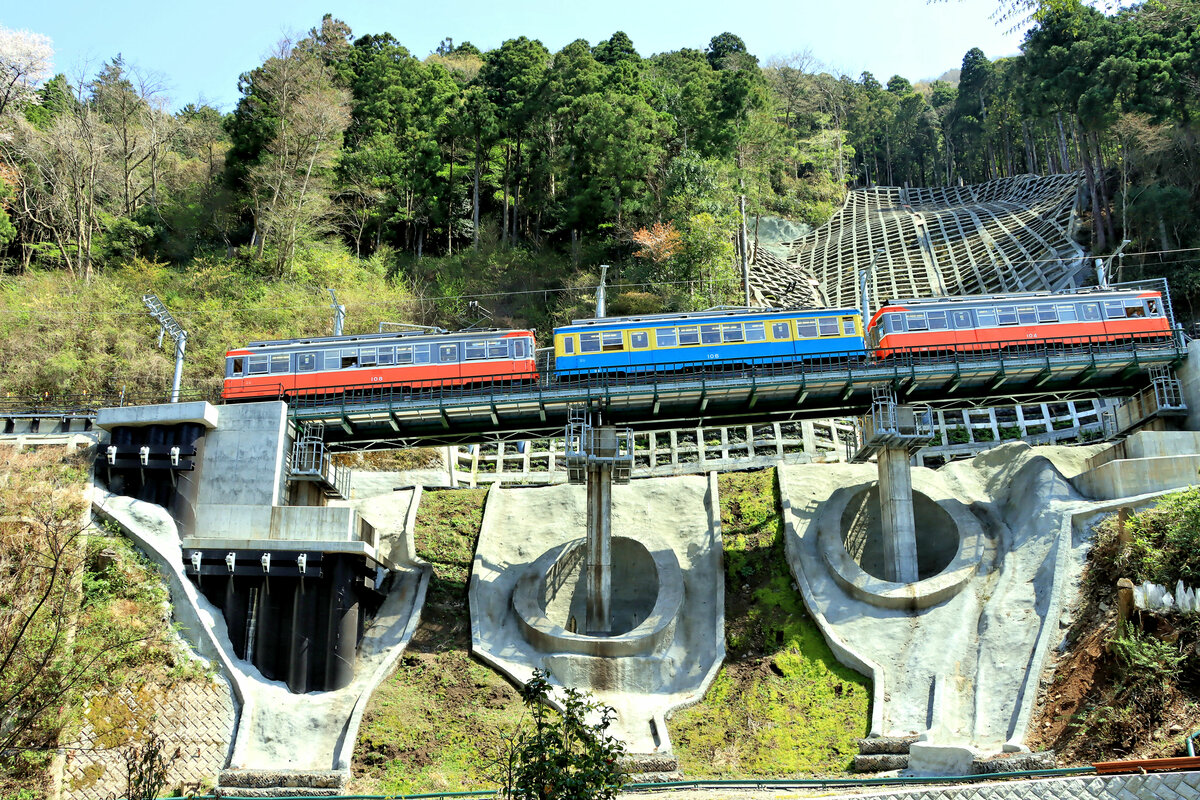 Die Hakone Tozan Bahn wurde mehrmals von schweren Erdbeben (v.a. 1923), Regenstürmen und Taifunen heimgesucht. Besonders schlimm traf es die Bahn am 12. und wieder am 25.Oktober 2019, wo ein ganzer Berghang abrutschte und einen erheblichen Teil der Strecke unter sich begrub; erst am 23.Juli 2020 konnte die ganze Strecke wieder befahren werden. Im Bild befährt eine alte Komposition mit den Triebwagen 108, 106 und 104 die wieder aufgebaute Stelle unterhalb Kowakidani. 12.April 2022  

