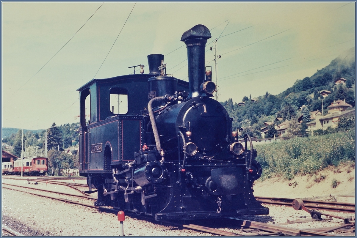 Die kleine, 5,1 Meter lange Dampflok G 3/3 N° 1  Le Doubs  rangiert in Blonay.

Sie wurde 1890 unter der Fabriknummer 618 von der SLM gebaut, und mit zwei weiteren an die  R-d-B (Régional des Brents) geliefert, wo sie bis zur Elektrifizierung der Strecke Le Locle - Les Brents 1950 ihren Dienst versah. In der Folge wurde die Lok der SBB übergeben, mit dem Zweck, sie dem Verkehrshaus der Schweiz in Luzern weiter zu reichen, wobei dann die Lok ab 1973 Leihweise zur Blonay-Chamby Bahn kam. Ab 1976 ging sie in den Besitz der B-C über. Interessanterweise scheinen auch die beiden anderen Lok G 3/3 N°2  Le Père Frédéric und die G 3/3 N° 3  Les Brenets  der Nachwelt erhalten geblieben zu sein. 

Die Lok wurde als leichte Strassenbahnlok mit nur 15 - 16 Tonnen Dienstgewicht gebaut. Die Zylinder arbeiteten zur Vermeidung zu grosser Seitenausladung direkt auf die entsprechend ausgebildete Kuppelstange. Weitere Loks wurden (z.T auch von Krauss&Co München) an folgende Bahnen geliefert: WB (Waldenburgerbahn), FW (Frauenfeld- Wilbahn) und P-S-C (Pont Sage La Chaux de Fondsbahn). (Quelle der Dampfbetrieb der Schweizer Eisenbahnen 1847 - 1966) von Alfred Moser)

Die Analogaufnahme stammt vom August 1985