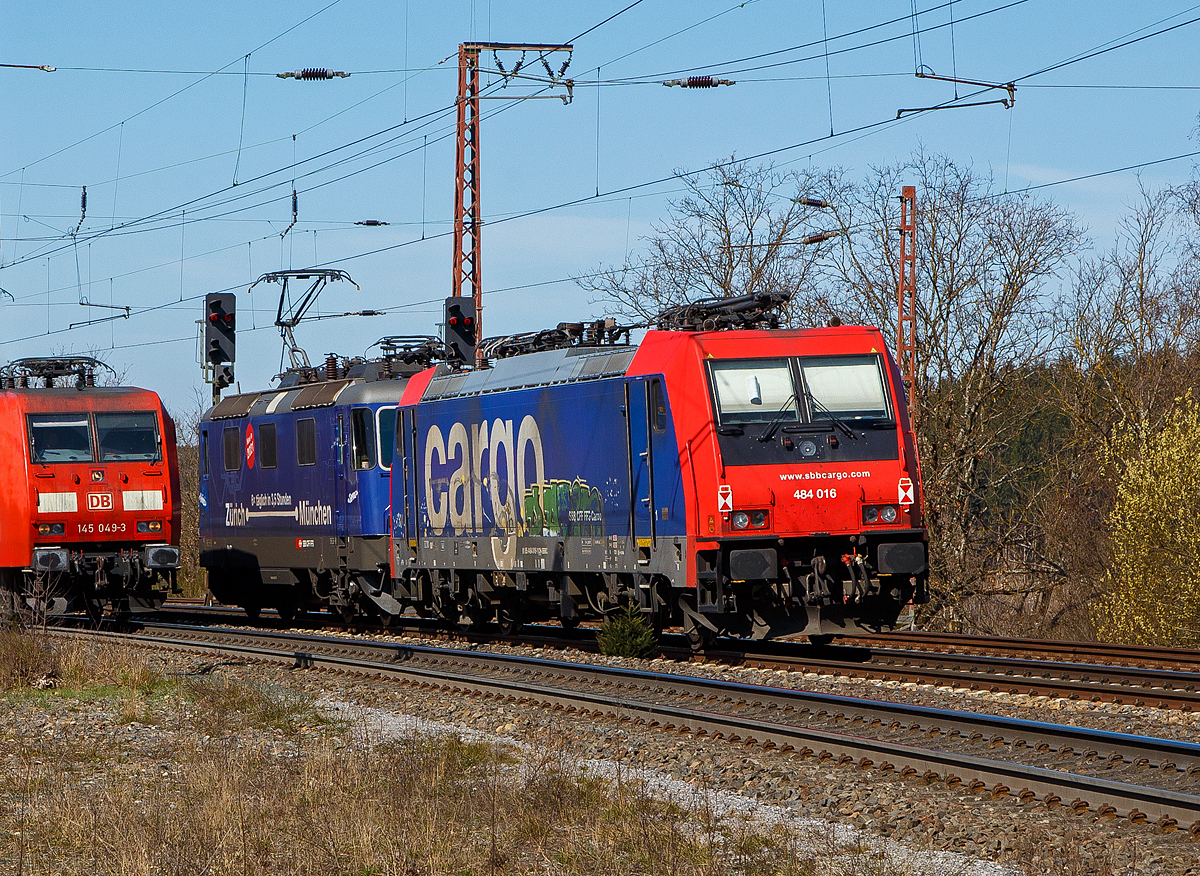 Die SBB Cargo Re 484 016-1(91 85 4484 016-1 CH-SBBC), ex E 484.016 SR, eine TRAXX F140 MS, geschleppt am Haken der SBB Cargo Re 421 371-6 (91 85 4421 371-6 CH-SBBC), ex Re 4/4 II 11371, mit Werbung Zürich – München 6 x täglich in 3,5 Stunden, haben am 30.03.2021 in Rudersdorf (Kr. Siegen) Hp 0, bevor es in Richtung Siegen weitergeht. Links kommt gerade in Gegenrichtung die DB 145 049-3 mit einem Containerzug. Eigentlich ist komplette Dillstrecke (KBS 445) zweigleisig, aber hier ist wohl ein Gleis gesperrt. 

Eine SBB Cargo Re 484 wie die 016-1 kann man eigentlich Deutschland nur mit viel Glück sehen, denn sie haben nur die Zulassungen für die Schweiz und Italien. Sie haben keinen Stromabnehmer mit breiterer Wippe gemäß deutscher Vorschrift, auch die die deutsche Zugsicherung Indusi fehlt ihnen. Der Lz war auf dem Weg nach Krefeld.

Lebensläufe:
Die Re 421 371-6 wurde 1983 von der SLM Winterthur (Elektrik BBC/ SAAS) unter der Fabriknummer 5235 gebaut und als Re 4/4 II 11371 an die SBB geliefert. Im Jahr 2002 erfolgte der Umbau zur Re 421 für die SBB Cargo (Einsatz auch in Deutschland). Die zugelassene Höchstgeschwindigkeit für die Schweiz beträgt 140 km/h und für Deutschland 120 km/h.

Die Re 484 016-1 eine Bombardier TRAXX F140 MS wurde 2004 von Bombardier in Kassel unter der Fabriknummer 34009 gebaut und an die SBB Cargo AG, als E 484.016 SR geliefert.

