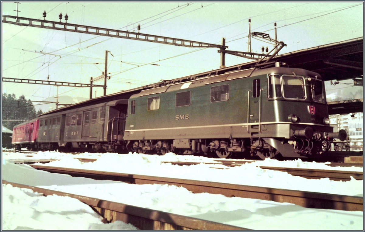 Die SMB Re 4/4 III 181 wartet mit ihrem Regionalzug nach Solothurn in der Zugsausgangsstation Moutier auf die Abfahrt. 
Interessant ist der Reisezugwagen hinter der Lok, welcher auch über ein Gepäckabteil verfügt. 

Analogbild vom 23. Feb. 1985
