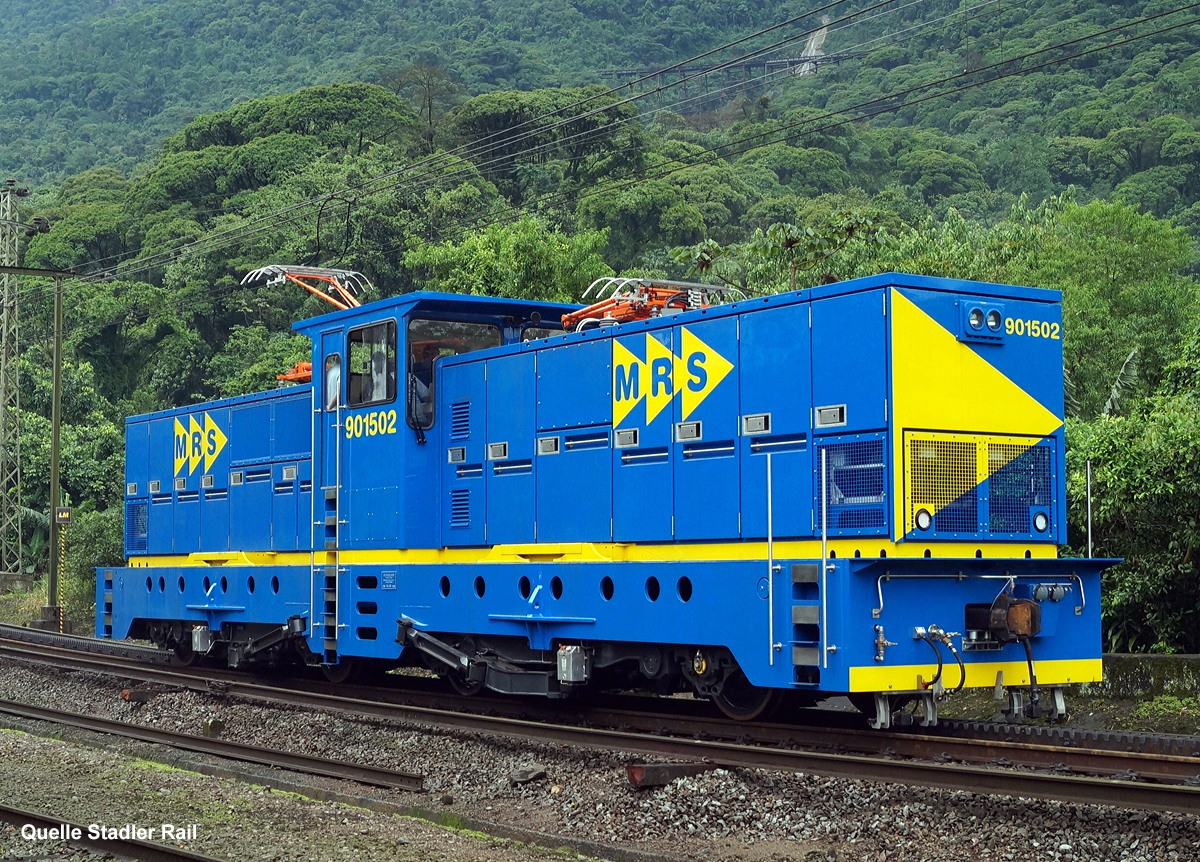 
Die stärksten Zahnradlokomotiven der Welt, die Stadler He 4/4 901502 der MRS Logística S.A. am 23.10.2012 solo bei Raiz da Serra. 
Das Bild wurde mir freundlicher Weise von Stadler Rail zugesandt und für eine Veröffentlichung hier überlassen.  

Die Stadler He 4/4 ist eine gemischte elektrische Zahnrad-Adhäsions-Lokomotive He 4/4 von den 2012 sieben Stück für MRS Logística S.A. in Brasilien gebaut wurden. Es besteht eine Option für drei weitere Lokomotiven.

Die MRS Logística S.A u.a. die  Eisenbahnlinie von Jundiaí  über São Paulo nach dem Hafen von Santos, das Einsatzgebiet der Loks ist der ca. 10 km lange Zahnstangenstrecke zwischen Raiz da Serra auf 17 m NN (ca. 20 km von Santos) nach Paranapiacaba auf 810 m NN. Die Maximale Neigung der Strecke beträgt hier 103 ‰. Die Strecke mit einer Spurweite von 1.600 mm (Irische Breitspur) ist hier mit einer Zahnstange des Systems Abt mit drei Lamellen je 60 mm Breite und mit einer Oberleitung mit 3000 Volt Gleichstrom ausgerüstet.  Das Lichtraumprofil der Lokomotiven ist größer als bei den anschließenden Adhäsionsstrecken, so dass die Lokomotiven nur zwischen Raiz da Serra und Paranapiacaba eingesetzt werden und die Hauptwerkstätten der MRS Logística S.A. nicht ohne weiteres erreichen können. Sie haben deshalb vor Ort eine eigene Werkstätte.

Das Transportvolumen der Strecke beträgt ca. 14 Mio. Bruttotonnen im Jahr (das entspricht etwa der Hälfte des Gotthardtunnels). Das Transportgut fällt überwiegend talwärts an, zu 80 % handelt es sich um Eisenerz sowie landwirtschaftliche Produkte. Da nur die Lokomotiven mit Bremszahnrädern ausgerüstete sind, befinden sich diese aus Sicherheitsgründen immer auf der Talseite. Das heißt also, die Züge werden die Strecke hinauf geschoben. Die alten Hitachi Lokomotiven dürften aus Sicherheitsgründen nur in Doppeltraktion verkehren.

Es ist eine Doppeltraktion zweier Lokomotiven vorgesehen. Dies erlaubt, als Vorstelllast einen Zug mit einem Gewicht von 850 Tonnen zu befördern. So werden mit diesen Lokomotiven 50 % mehr Last, bei höherer Geschwindigkeit, als mit den über 40 Jahre alten Lokomotiven von Hitachi gebaute Lokomotiven transportiert.  Einzel kann eine Stadler He 4/4 einen 750 t Zug befördern.

Die speziell für den harten Betriebseinsatz (7 Tage/Woche,24 h)  von Stadler entwickelten Lokomotiven verfügen über eine Leistung von 5.000 kW, die Fahrleitungsspannung  beträgt  3kV  DC,  die Bremsenergie  kann  rekuperiert  werden. Die Lage des Zahnrades kann entsprechend der Abnützung der Räder nachgestellt werden

Die gemischte Zahnrad-Adhäsion-Lokomotive Stadler He 4/4 hat zwei zweiachsige einzelachsangetriebene Drehgestelle mit zusätzlich je zwei Antriebszahnrädern, also mit der Achsfolge Bozz' Bozz'. Jedes Drehgestell hat somit zwei Adhäsion- und Zahnradmotoren. Jede Lok besteht elektrisch aus zwei unabhängigen Antriebseinheiten, so ist eine hohe Redundanz gegeben. Zudem erfolgt eine Rückspeisung des Bremsstroms in die Oberleitung.

Die Lokomotive besitzt einen Mittelführerstand mit zwei schmäleren Vorbauten. Der klimatisierte Führerstand hat eine Fußbodenhöhe von 2.450 mm und ist damit so hoch wie möglich angeordnet, damit der Lokomotivführer bei Bergfahrt über die vorgestellten Wagen blicken kann. Der Lokomotivführer sitzt vor einem quer zur Fahrrichtung eingebauten Führerpult und kann seinen Sitz in die Fahrtrichtung drehen. Auf jedem Vorbau ist über dem Drehpunkt des Drehgestells jeweils ein mit drei Schleifstücken versehener Stromabnehmer montiert. Die Vorbauten sind um die Höhe des abgesenkten Stromabnehmers niedriger als das Führerhaus ausgeführt. Damit liegen Vorbauten, Stromabnehmer und Führerhaus im gleichen Lichtraumprofil.

Die Lokomotive besitzt für jede angetriebene Achse und jedes Zahnrad einen eigenen Motor, es gibt somit insgesamt acht Fahrmotoren. Bei der Fahrt im Zahnstangenabschnitt arbeiten die Adhäsionsmotoren mit und erbringen so rund 25 % der Zug- oder Bremskraft. Die Primärfederung ist wegen des Zahnradantriebes sehr steif ausgeführt. Die Höhe des Zahnradeingriffes kann durch Unterlegen von Beilageplatten an die Abnutzung der Antriebsräder angeglichen werden. Die Drehgestelle sind verwindungsweich ausgeführt und besitzen Gleitlager am mittleren Querträger. Der Rahmen der Lokomotive ist auf eine Längsdruckkraft von 5.000 kN ausgelegt.

Bergseitig ist die Einspeisung von einer externen Diesel- Generatorgruppe möglich. Damit kann der Gleisunterhalt mechanisiert und Fahrdrahtunabhängig durchgeführt werden.

TECHNISCHE DATEN der He 4/4:
Nummerierung: 	901501–901507
Anzahl: 7
Hersteller: 	Stadler Rail
Baujahre: 	2012
Spurweite: 	1.600 mm (Irische Breitspur)
Achsformel: Bozz' Bozz'
Länge über Kupplung: 18.720 mm
Höhe: 4.600 mm
Breite: 3.280 mm
Drehzapfenabstand: 	8.300 mm
Achsabstand im Drehgestell: 5.000 mm (Zahnräder  3.420 mm)
Dienstgewicht: 121 t
Höchstgeschwindigkeiten: 60 km/h (Zahnrad bergwärts 30 km/h, talwärts 25 km/h)
Leistung am Rad: 5.000 kW
Anfahrzugkraft: 760 kN (Adhäsion 240 kN, Zahnrad 520 kN)
Dauerzugkraft:  540 kN
Treibraddurchmesser: 	1.069 mm (Neu)
Zahnradsystem: 	Abt dreilamellig je 60 mm Breit
Anzahl Antriebszahnräder: 	4
Größe Zahnräder: 1.031 mm
Stromsystem: 3000 Volt =
Stromübertragung: Oberleitung
Gefälle: 104 ‰
Kupplung: Standard AAR-Kupplungen

Quelle Stadler Rail und Wikipedia. 
Dank an Stadler Rail

