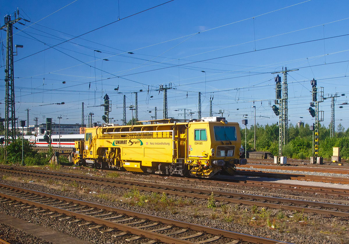 
Die Universal-Stopfmaschine Unimat-Sprinter ESM 865 der DB Netz AG (Schweres Nebenfahrzeug Nr.  97 43 52 004 17-6) ist am 01.06.2017 bein Bahnhof Hamm (Westf.) abgestellt (Bild aus einem Zug heraus).

Die Stopfmaschine (ESM – 08 – 275 / Sprinter) wurde 2000 von Plasser & Theurer unter der Fabriknummer 1164 gebaut und an die DB Netz AG geliefert..

Die 08-275 UNIMAT-Sprinter sind eine speziell für die Einzelfehlerbehebung entwickelte Stopfmaschine. Sie ist mit zwei Weichenstopfaggregaten mit jeweils vier Schwenkpickeln zur universellen Bearbeitung von Strecken und Weichen ausgestattet. Das kombinierte Hebe- und Richtaggregat besteht aus einem Hebehaken, einer Richtrolle und einer Rollhebezange pro Schienenstrang. Für eine schnelle Überstellung zur Baustelle ist die Maschine mit einem hydrodynamischen Antrieb für eine Höchstgeschwindigkeit von 100 km/h ausgelegt. Flankenpflüge, die im Bereich des vorderen Drehgestells montiert sind und eine Kehrbürste am hinteren Ende der Maschine, sorgen nach den Stopfarbeiten für die Herstellung des geforderten Schotterprofils. So ist sie eigentlich eine Stopfmaschine und Schotterpfug.
