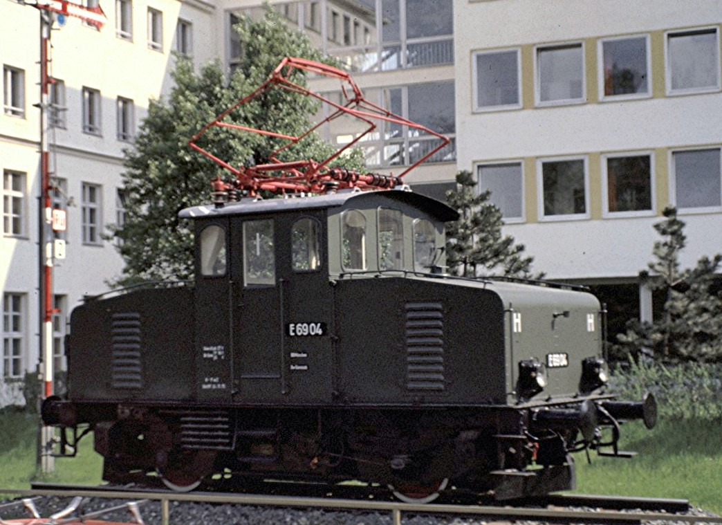 E 69 04 in Mnchen auf einem Sockel vor der Oberpostdirektion, aus einem geffneten Oberlicht einer fahrenden Strassenbahn fotografiert, am 26.05.1979 (Diascan).