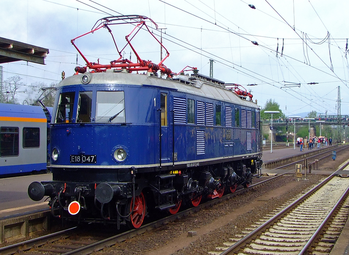 E18 047 (DB 118 047-0, eingestellt als 91 80 6118 047-0 D-MEG) fährt am 01. Mai 2010 durch den Bahnhof Bebra.

Die Schnellzug-Elektrolokomotive wurde 1939 bei AEG unter der Fabriknummer 5161 gebaut.
Die Elektrolokomotiven der Baureihe E 18 (ab 1968 DB-Baureihe 118), gehörten zu den schnellsten Elektrolokomotiven der Deutschen Reichsbahn-Gesellschaft (DRG). Sie erreichte eine Höchstgeschwindigkeit von 150 km/h. Achsanordnung ist 1 Do' 1
Die Maschine ist im Besitz des Verkehrsmuseums Nürnberg.

Lebenslauft und Bezeichnungen:
1939-1949: DRB E 18 047 (Deutsche Reichsbahn)
1949-1968: DB E 18 047
1968-1984: DB 118 047-0
1984-1997: als Museumslok DB E 18 047 (BSW-Gruppe Würzburg)
1997-2005:  E 18 047 (DB Museum)
seit 2005: E 18 047 (DB Museum Nürnberg, Außenstelle Halle/Saale, eingestellt durch die MEG - Mitteldeutsche Eisenbahn GmbH (DB Cargo Tochter)

Die Lokomotiven der Baureihe E 18 waren bestimmt zur Beförderung schwerer Schnellzüge mit hohen Geschwindigkeiten. Die Lokomotiven wurden für die neu elektrifizierten Strecken München-Stuttgart und München-Nürnberg-Leipzig-Berlin entwickelt.

Im normalen Schnellzugdienst konnten die Maschinen 935-t-Schnellzüge in der Ebene mit 140 km/h, 990-t-Züge bei 5 Promille mit 100 km/h, 600-t-Züge bei 10 Promille mit 100 km/h und 360-t-Züge bei 20 Promille mit 75 km/h befördern.

Viele Baugruppen, wie zum Beispiel die Motoren oder der AEG Federtopfantrieb, wurden von der E 04 übernommen. Der Lokkasten hingegen war eine Neuentwicklung, der den Grundsätzen der Aerodynamik und der Stromlinie Rechnung trug. Die E 18 hatte keinen genieteten, sondern einen geschweißten Fahrzeugrahmen. Die Laufachsen waren für die Laufruhe mit der jeweils ersten – verschiebbaren – Treibachse in einem AEG-Kleinow-Gestell zusammengefasst. Der Antrieb erfolgte über Federtöpfe. Jeder Radsatz wurde über den verstärkt ausgeführte Kleinow-Federtopfantriebe von hochgelagerten Gestellmotoren Typ EKB860 angetrieben. Die ursprünglichen der Stirnfront angepassten Leuchten wurden bei der DB bis auf wenige Ausnahmen durch Einheitsleuchten ersetzt. 

Bedingt durch den Zweiten Weltkrieg wurde die weitere Beschaffung der E 18 zugunsten der wichtigeren Kriegsloks E 44 und E 94 eingestellt. Bis Kriegsende wurden daher nur 53 Lokomotiven gebaut. Nach dem Krieg verblieben bei der Deutschen Bundesbahn 41 Lokomotiven, die weiterhin im Schnellzugdienst eingesetzt wurden. Obwohl die Lokomotiven sich erwartungsgemäß gut bewährten und gute Laufeigenschaften auf geraden Strecken hatten, konnten sie im Bogenlauf nicht überzeugen und dieser war durch Reibung sogar teilweise ruckartig. Die optimale Einstellung der Hohlwellen und gute Wartung verbesserten die Laufgüte der Loks. Auch der spätere Einbau von Gummi-Parabelfedern statt der Federtöpfe brachte eine Verbesserung.

Mitte der sechziger Jahre wurden die leistungsfähigen Lokomotiven durch die neu in Auslieferung befindlichen E 10 verdrängt. Die Loks wurden nun vermehrt im Nahverkehr eingesetzt, was der Schnellzuglok nicht sonderlich bekam. Die Schäden an Schaltwerk und Bremse häuften sich. In den siebziger Jahren erhielten einige E 18 die Vorrüstung für die automatische Kupplung. Es wurden sogenannte Verschleißpufferbohlen angebracht, die das elegante Aussehen der Loks nachteilig beeinflussten. 

TECHNISCHE DATEHN:
Spurweite:  1435 mm (Normalspur) 
Achsformel:  1'Do1'
Länge über Puffer:  16.920 mm
Achsabstände: 2.800 / 2.100 / 3.000/  2.100 / 2.800 mm
Treibraddurchmesser: 	1.600 mm
Laufraddurchmesser: 	1.000 mm
Dienstgewicht:  108,5 t
Radsatzfahrmasse:  18,1 t
Höchstgeschwindigkeit:  150 km/h
Stundenleistung:  3.040 kW
Dauerleistung:  2.840 kW
Anfahrzugkraft:  206 kN
Treibraddurchmesser:  1.600 mm
Stromsystem:  15 kV 16 2/3 Hz AC
Anzahl der Fahrmotoren:  4 (Gestellmotore Typ EKB86
Antrieb:  Kleinow-Federtopfantrieb
Kupplungsart: Schraubenkupplung
