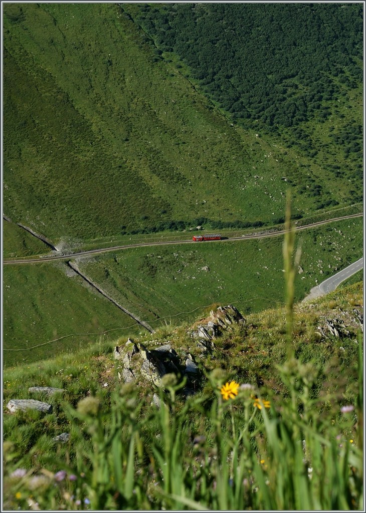 Eigentlich ein Bahnsuchbild, doch die paar Pixel DFB-Rot des Tm und B im Tal fallen sofort auf...
Ein Blick von der Furka Passs Strasse auf den Dienstzug auf dem Weg Richtung Realp. 
5. Aug. 2013