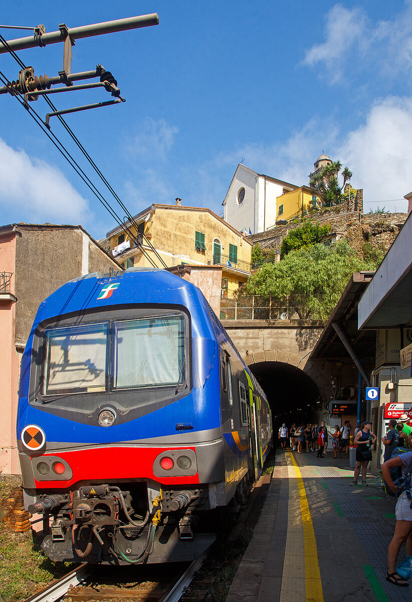 Ein Trenitalia Doppelstockzug (gezogen von einer E.464) hat am 22.07.2022, als Cinque Terre Express (Regionale) von La Spezia, via Riomaggiore, Manarola, Corniglia, Vernazza, Monterosso, nach Levanto, den Cinque Terre Bahnhof Vernazza erreicht. 

Vernazza ist eines der fünf Dörfer der Cinque Terre (Fünf Ortschaften) und verfügt, wie die anderen Dörfer, über einen Bahnhof an der Bahnstrecke Pisa–Genua (RFI Strecke-Nr. 77 / KBS 31 La Spezia–Genua). Der Bahnhof liegt zwischen zwei zweigeteilten Tunneln, jeder Bahnsteig hat seine eigenen Tunnelröhren. Wie auch in Riomaggiore passen die Bahnsteige nicht komplett unter freien Himmel, der Rest der Bahnsteige ist jeweils in einem der Tunneln. 

Oben die Kirche San Francesco (Chiesa di San Francesco) vom gleichnamentlichen Kloster Convento di San Francesco, welches hinter der Kirche liegt.
