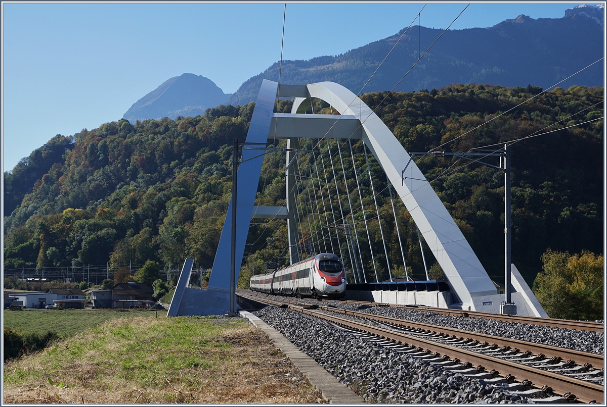 Fast 23 Meter über die Gleise wölbt sich die beiden Bögen der SBB Brücke  Massogex , die zwischen Bex und St-Maurice über die Rhone führt. Die Brücke weist eine Spannweite von  125.8 Meter auf und gilt als längste Stählerne Eisenbahnbrücke der Schweiz. Sie ersetzt seit 2016 die beiden aus den Jahren 1903 und 1924 stammenden eingeleisigen Stahlbrücken. (Tech. Ang. Quelle: TEC21 Nr 41).
Das Bild zeigt einen SBB ETR 610 der Als EC 32 von Milano nach Genève unterwegs ist.
11. Okt. 2017