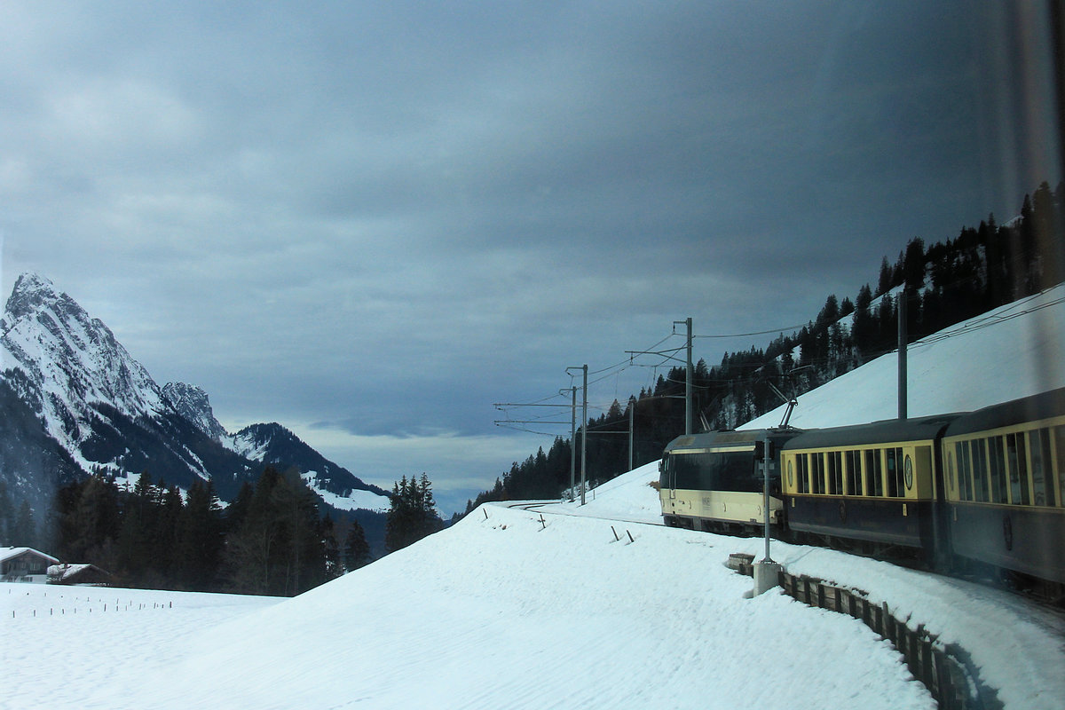 Heutzutage ist es fast unmöglich, ohne Spiegelungen aus dem Zug heraus zu photographieren. Beim Aufstieg hoch über dem Saanenland von Gruben nach Schönried gelang es irgendwie, Lok 8001 einzufangen, aus einem der erkerartig herausragenden Fenster eines Belle Epoque-Wagens. 4.Februar 2021 