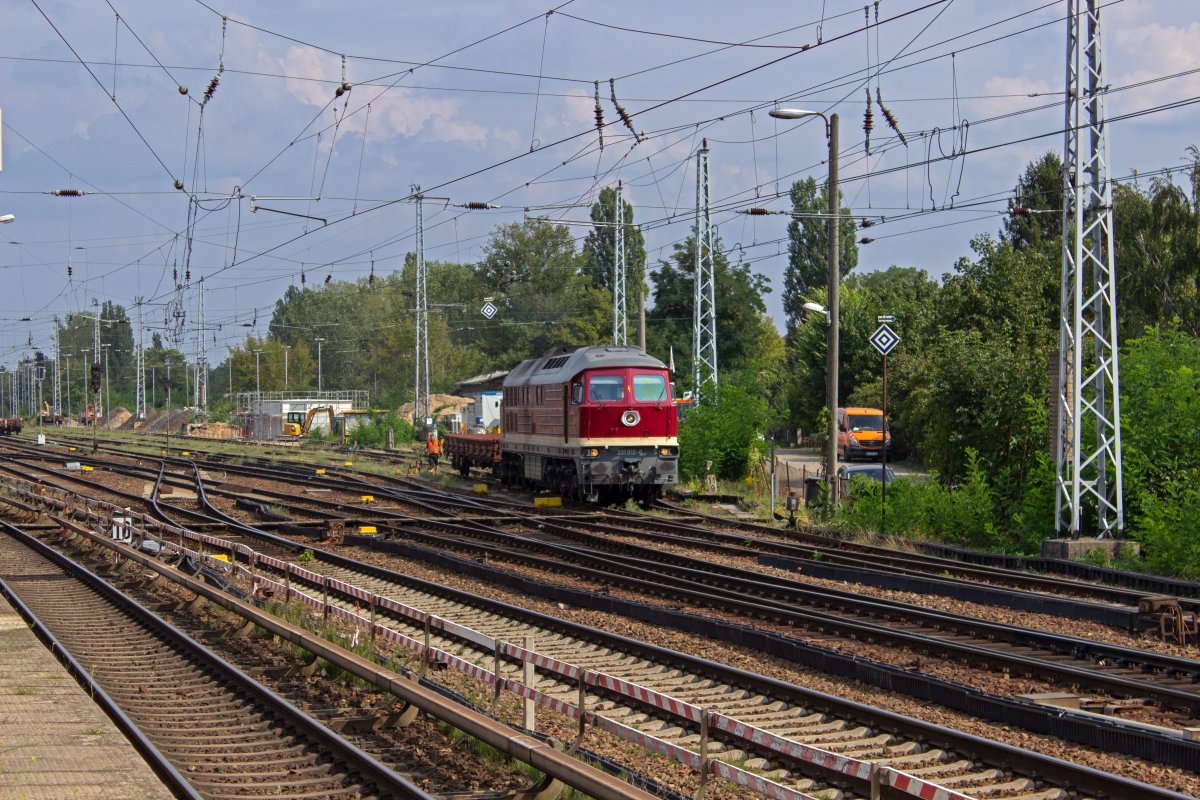 In Berlin-Köpenick wird in Vorbereitung auf den Umbau des Bahnhofs gebaut. Der alte Güterschuppen war der für einen neuen Fernbahnsteig nötigen Verschiebung einiger Gleise im Weg und ist bereits verschwunden. Vor dem unscheinbaren Betonkasten der ESTW-Schaltanlage rangiert 231 012 der WFL einen Güterwagen der Baustellenlogistik.