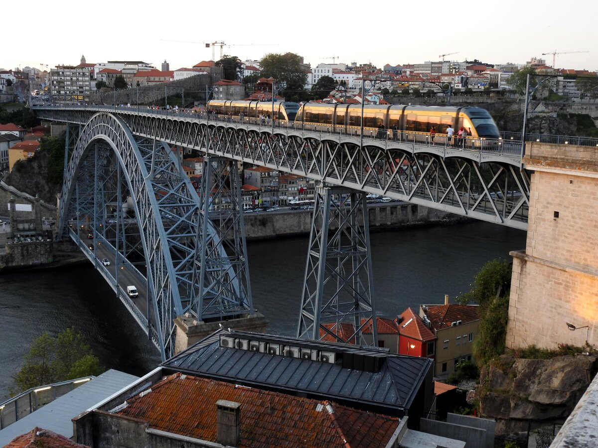 Metro Doppeltraktion auf der Brücke Ponte Luiz I bei Sonnenuntergang (Spiegelung in den Scheiben der Metro) am Jardin do Morio in Porto am 16.05.2018.