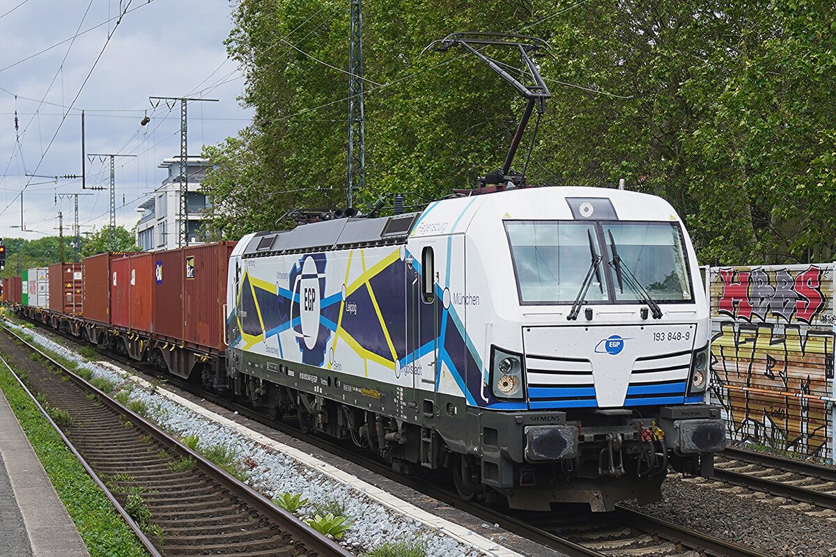 Mit einer bis auf eine Stelle volbeladener Containerzug durchfahrt EGP 193 848  am verregneten 13 Mai 2026 K�ln S�d. K�ln S�d lohnt sich beinahe immer f�r ein Besuch wann Mann G�terz�ge anschauen will, aber es gibt leider auch ein Larmschutzwand annex Grafftititr�ger.