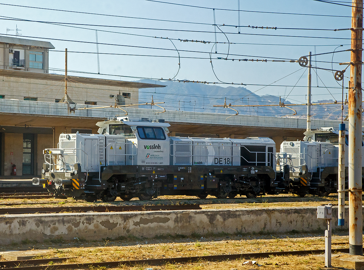 Neue Verschub-Lokomotiven fürs Trajekt-Manöver an den Ufern der Straße von Messina....
Die DE 18 2421  Barbara  alias 2318005-1 I-IMTI (92 83 2318 005-1 I-IMTI) der MIST - Mercitalia Shunting & Terminal S.r.l. íst am 20.07.2022 beim Bahnhof Messina Centrale abgestellt. 

Die vierachsige (Bo'Bo') dieselelektrische DE 18 wurde 2020 von Vossloh unter der Fabriknummer 550 2421 gebaut und im März 2021 von Kiel nach Italien überführt. Sie ist Eigentum der Vossloh Locomotives GmbH und an die MIST - Mercitalia Shunting & Terminal S.r.l. vermietet. Sie sind für Manöver von Zügen auf die Eisenbahnfähren, wobei im Einsatz konnte ich nur die RFI D.145.2000 sehen. Sie hat d. Z. nur die Zulassung für Italien. 

Die Vossloh DE 18 ist eine diesel-elektrisch angetriebene Lokomotive für den schweren Rangier- und Streckendienst mit der Achsfolge Bo'Bo'. Es handelt sich um die erste Lokomotive aus dem ehemaligen MaK-Werk Kiel seit der Einstellung der Produktion der DE 1002 im Jahr 1993. Etwa 60 % der Bauteile der DE 18 sind mit denjenigen der diesel-hydraulischen Variante G 18 deckungsgleich. Die Konstruktion des Fahrzeuges entspricht nach Herstellerangaben der Crash-Norm EN 15227. Einsatzbereit mit mehreren europäischen Länderzulassungen nach TSI hat sich die vierachsige Universallokomotive als hochmoderner Branchenstandard etabliert. Bei Geschwindigkeiten zwischen 17 und 120 km/h bietet die DE 18 kontinuierlich eine Leistung von 1.800 kW, was sie zur aktuell leistungsstärksten Mittelführerhauslokomotive auf dem europäischen Markt macht.

TECHNISCHE DATEN:
Spurweite:  1.435 mm 
Achsfolge:  B‘B‘
Länge über Puffer : 17.000 mm  
Drehzapfenabstand: 7.940 mm
Achsabstand im Drehgestell: 2.400 mm
Raddurchmesser:  1.000 mm (neu) / 920 mm (abgenutzt)
Größte Höhe:  4.310 mm  
Größte Breite:  3.080 mm
Höchstgeschwindigkeit: 120 km/h
Dieselmotor Typ:  MTU 12V 4000 R43L 
Dieselmotorleistung:  1.800 kW (2.447 PS) bei 1.800 U/min
Leistungsübertragung: elektrisch
Stromrichter : IGBT
Traktionsmotoren: 4 Stück Drehstrom-Asynchronmotoren vom Typ VEM DKLBZ 3510-4
Leistung am Rad: 1.440 kW
Anfahrzugkraft:  300 kN
Dauerzugkraft: 230 kN bei 24.2 km/h
Dienstgewicht:  90 t
Kraftstoffvorrat:  4.000 l
Elektrodynamische Bremsleistung: max. 1.450 kW  
Bremse: 2 x KE-GP-E mZ (D)
Kleinster befahrbarer Bogenradius:  55 m
Fährbootwinkel: 1° 30’ (bei dieser Lok wichtig)

Weitere Motordaten (MTU 12V 4000 R43L):
Dieselmotorart: 12 Zylinder -Viertakt-90°-V-Dieselmotor mit Abgasturboaufladung, Ladeluftkühlung und Common-Rail-Einspritzung
Motorhersteller: Motoren- und Turbinen-Union Friedrichshafen (MTU)
Motorhubraum: 57.2 l (Ø 170 mm Bohrung x 210 mm Hub)
Motorabmessungen: 2.386 x 1.562 x 2.015 mm
Motorgewicht: 6.613 kg (trocken)
Abgasvorschriften:  EU/2004/26 Stufe IIIA/prepared for stage IIIB  