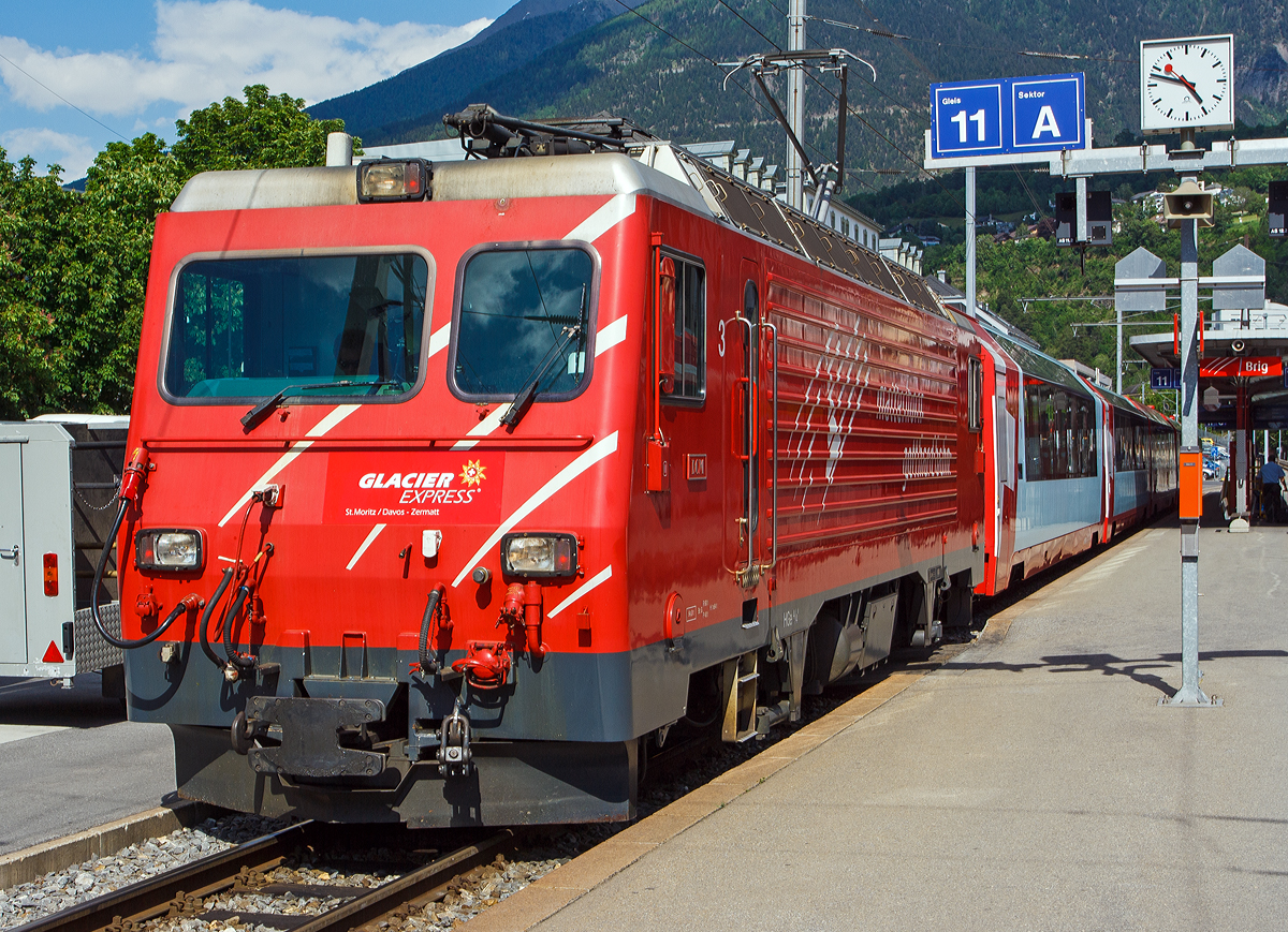 
Neue Version in 1200px....
Die MGB HGe 4/4 II - 3   Dom  (ex BVZ 3   Dom )  steht am 28.05.2012 mit Glacier Express im Bahnhof (-vorplatz) von Brig. 

Der Taufname  Dom  bezieht sich auf den in den Walliser Alpen liegenden Berg Dom (4.545 m ü. M.). Die MGB HGe 4/4 II - 3  Dom  wurde von SLM (Schweizerische Lokomotiv- und Maschinenfabrik) in Winterthur 1990 unter der Fabriknummer 5421 gebaut und an die Brig-Visp-Zermatt-Bahn (BVZ) geliefert. Der elektrische Teil ist von ABB.

Die HGe 4/4 II ist eine schmalspurige (1.000 mm) gemischte Zahnrad- und Adhäsions-Lokomotive. Eine erste Serie von fünf Lokomotiven wurde gemeinsam von der Furka-Oberalp-Bahn (FO) sowie von der SBB für die Brünigbahn, die heute zur Zentralbahn (zb) gehört, beschafft. Da sich dieser Lokomotivtyp bewährte, wurden weitere elf Lokomotiven bestellt, und schließlich gab auch noch die Brig-Visp-Zermatt-Bahn (BVZ) fünf Loks in Auftrag.

Die HGe 4/4 II bespannt vor allem schwere Personenzüge, zum Teil im Pendelzugbetrieb. Bei der Zentralbahn bespannte sie bis 2012 alle Schnellzüge von Meiringen nach Luzern, bei der Matterhorn Gotthard Bahn die Züge des Glacier-Express. Weiter führen die Loks Pendelzüge Brig–Visp–Zermatt und seit der Eröffnung des Tunnels nach Engelberg Pendelzüge Luzern–Engelberg. Außerdem werden aushilfsweise Autopendelzüge durch den Furkatunnel geführt. Schließlich gehören neben weiteren Personenzügen auch diverse Güterzüge Visp–Zermatt sowie bis 2013 Disentis–Sedrun (NEAT-Baustelle) zum Aufgabengebiet.

Konstruktion:
Der Lokomotivkasten ist ein Stahlblechkasten mit gesickten Seitenwänden. Die asymmetrische Frontscheibe aus beheizbarem Verbundglas verbessert die Sicht für den Lokomotivführer. Die drei Dachelemente sind aus Aluminium. Die Pufferkräfte werden über Verstrebungen auf den ganzen Kasten übertragen, weshalb auf seitliche Maschinenraumöffnungen verzichtet werden musste. Der gesamte Kasten hat ein Gesamtgewicht von nur 5,9 Tonnen. Er kann ohne bleibende Deformation eine zentrale Druckkraft von 1000 kN aufnehmen.

Die Drehgestelle sind als geschweißte Hohlträgerkonstruktion mit zwei Längsträgern und einem kräftigen mittleren Querträger sowie zwei Kopftraversen ausgeführt. Sie haben einen Achsstand von 2980 mm, und die Flexicoilfedern stützen den Kasten auf die seitlich an die Längsträger angeschweißten Federwannen. Die Zug- und Druckkräfte werden durch seitlich angeordnete Stangen mit Sphärolastiklagern übertragen. Wegen des kurzen Achsstands sind die Fahrmotoren oberhalb des Drehgestellrahmens angebracht.

Für den Antrieb wurde erstmals der Differentialantrieb eingebaut, der es ermöglicht, im Zahnstangenbetrieb auch einen Anteil der Zugkraft über den Adhäsionsantrieb aufzubringen. Dies setzt wiederum eine Schlupfbegrenzung im Differentialgetriebe voraus, um ein Schleudern oder Gleiten der Räder zu verhindern. Da die zweilamellige Abtzahnstange (System Abt) der FO nicht die gesamte Zugkraft aufnehmen kann, ist die Mithilfe des Adhäsionsantriebs notwendig; dieser übernimmt einen Drittel der Zugkraft. Hätte sich der Antrieb nicht bewährt, wäre es zumindest am Brünig mit der Riggenbachzahnstange möglich gewesen, auf einen abkuppelbaren Adhäsionsantrieb zu wechseln. Dies war aber nicht notwendig, da das Differentialgetriebe zur vollen Zufriedenheit funktionierte.

Bremssysteme:
Dank der elektrischen Rekuperationsbremse ist eine gleichmäßige Beharrungsbremse bei der Talfahrt möglich.
Daneben ist eine normale automatische Druckluftbremse eingebaut, welche auch als Bremssystem I bezeichnet und im Regelbetrieb zum Halten des Zuges verwendet wird. Sie ist als Klotzbremse ausgeführt.
Weiterhin ist noch das Bremssystem II installiert, welches für Zahnradbahnen vorgeschrieben ist und es ermöglichen soll, den Zug nur mit Hilfe der Lokomotive im Zahnstangenabschnitt zum Halten zu bringen, wenn das erste Bremssystem ausfallen sollte. Dieses ist als federspeichergestütztes Bandbremssystem ausgelegt, welches direkt auf das Zahnrad wirkt. Bei Einsatz dieser Bremse treten enorme Kräfte auf, welche nur unter Kontrolle sind, wenn die Anhängelast bei der Talfahrt nicht zu groß ist.
Schließlich ist eine direkt wirkende Rangierbremse vorhanden, die sich der Bremsklötze des Bremssystems I bedient.
Die Lokomotive hat keine Handbremse, sondern wird mit Federspeicherbremsen gesichert.

Technische Daten, der HGe 4/4 II MGB (ex FO bzw. BVZ), die der zb weichen ab:
Spurweite: 1.000 mm
Achsformel: Bo'Bo'
Dienstgewicht: 64 t 
Achslast: 16 t
Länge über Puffer: 14'.776 mm 
Höchstgeschwindigkeit Adhäsion: 100 km/h
Höchstgeschwindigkeit Zahnrad: 40 km/h
Stromsystem: 11 kV 16.7 Hz
Anzahl der Motoren: 4
Adhäsions-Antrieb: Gelenkwelle
Antrieb Zahnrad: Differentialantrieb
Zahnradsystem:  Abt (zweilamellig)
Stundenleistung: 1.932 kW
Dauerleistung: 1.875 kW
Anfahrzugkraft: 230 kN (Adhäsion) / 280 kN (Zahnrad)
Anzahl Bremssysteme: 4
Bremsen: Rekuperation, Klotz, Federspeicher, Bandbremse
Anhängelast: 130 t (125 ‰)