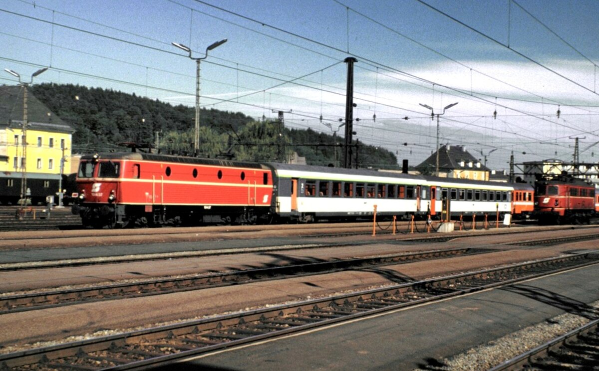 ÖBB 1044.57 mit EC Mozart; hinter der 1044 2 SNCF-EC Wagen, dann ÖBB EC-Wagen in Attnang-Puchheim; eine ÖBB 1018.04 wartet im Hintergrund am 05.10.1981.