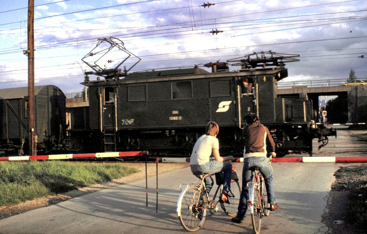 ÖBB 1080.11 in Attnang-Puchheim am Bahnübergang; die Jugend hat am Rangierbetrieb sichtbares Interesse am 07.10.1981.