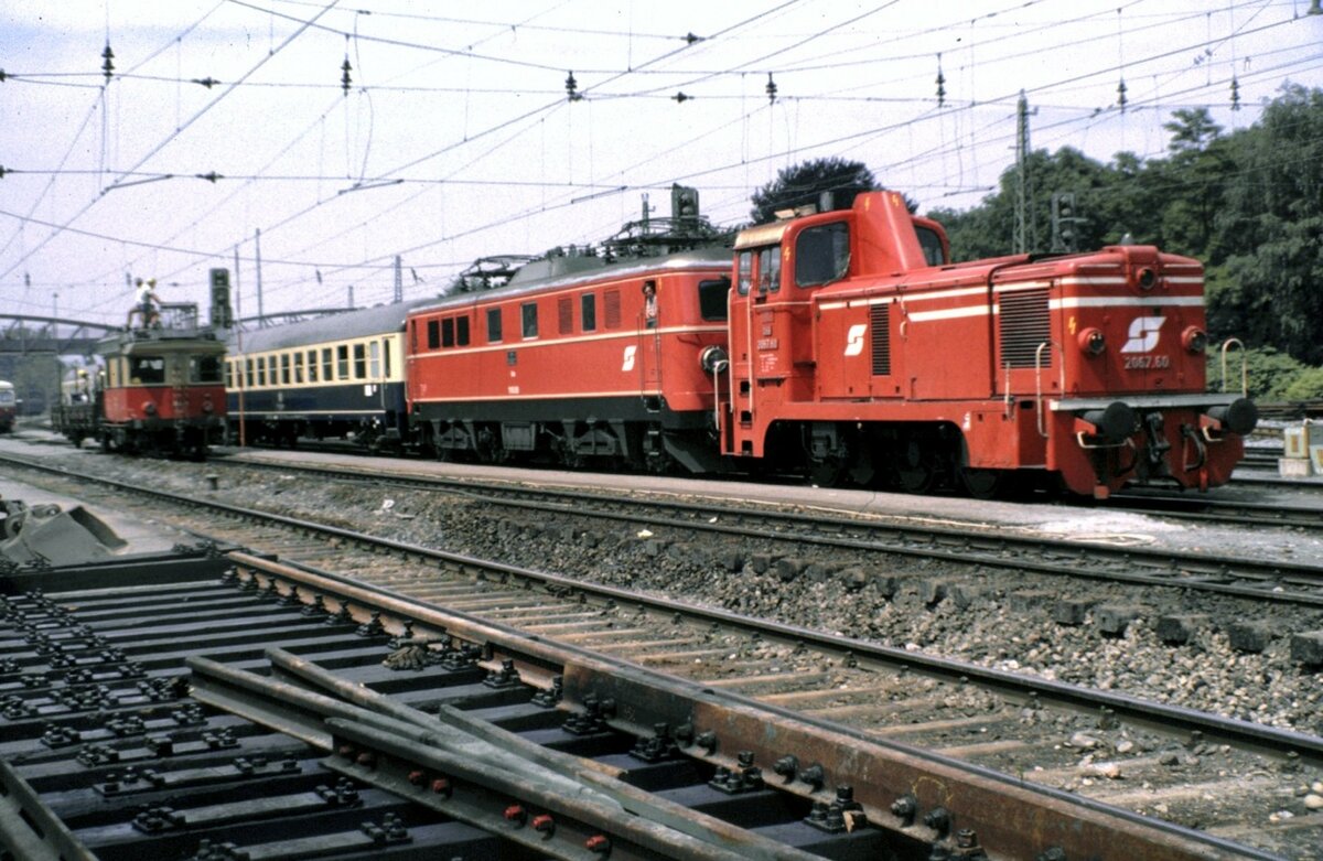 BB 2067.60 schleppt 1110.06 mit Zug aus stromlosen Bereich; im Hintergrund befindet sich ein Turmtriebwagen X 534 im Arbeiteinsatz in Bregenz am 12.06.1983.