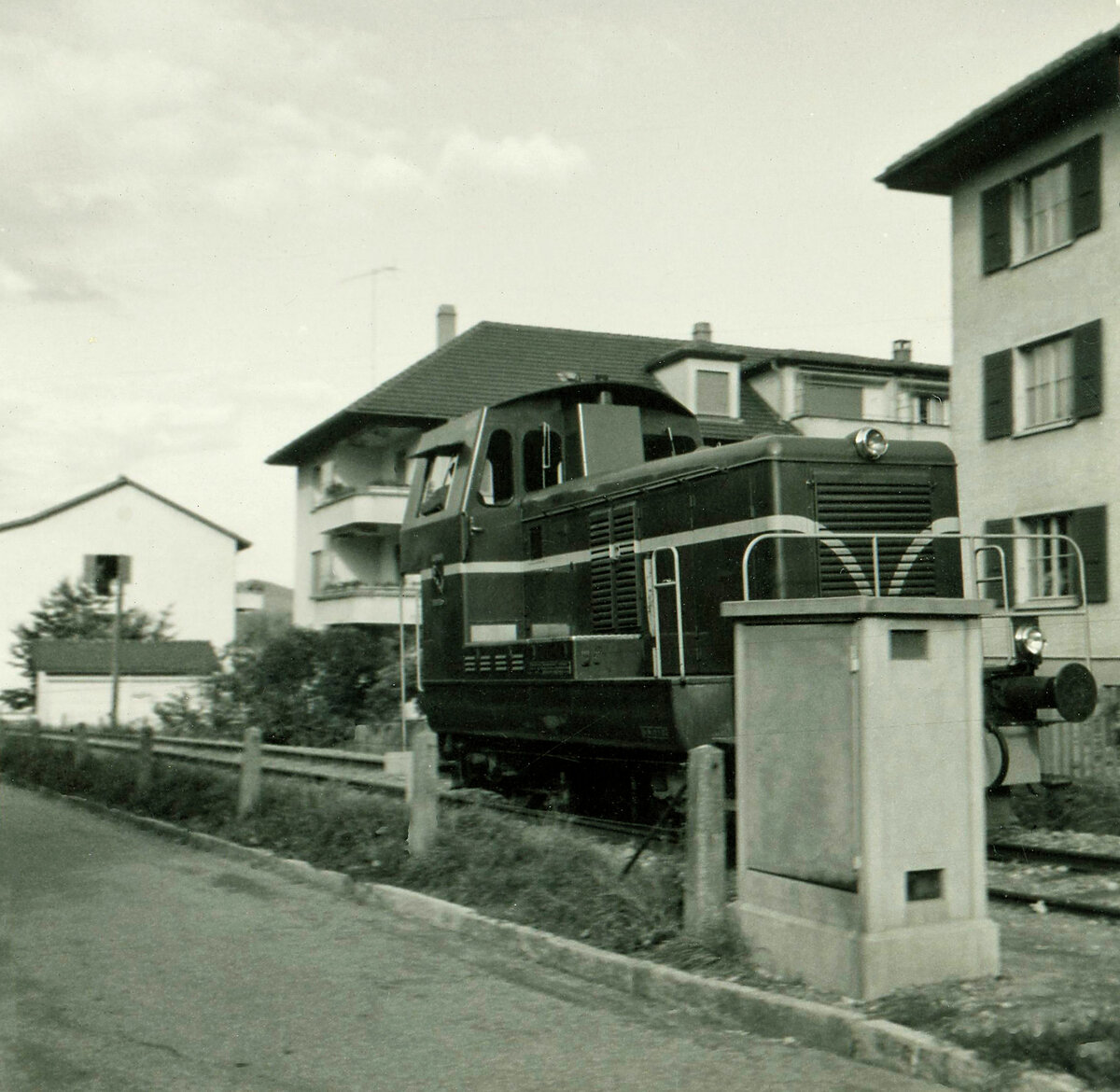 Unglücklicherweise von einem Kasten halb verdeckt zeigt diese Aufnahme von 1964 den Em 2/2  Mutz  der Gaswerkbahn Bern in umgekehrter Stellung gegenüber später, d.h. mit dem Führerstand talseitig. Unmittelbar nach Ueberquerung der Seftigenstrasse in Wabern. 