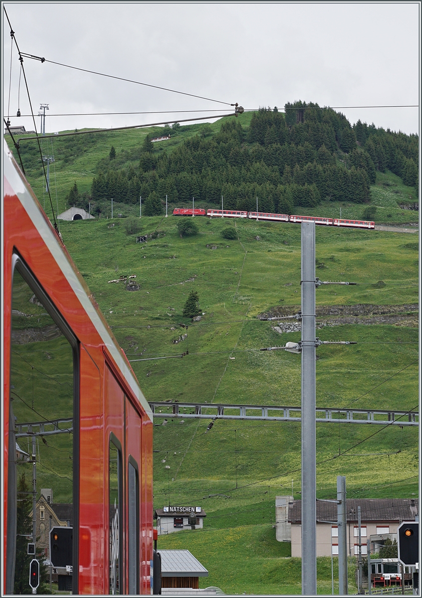 Während in Andermatt ein MGB Zug-Teil ins Bild ragt, kurvt hoch oben am Berg eine HGe 4/4 II mit ihrem Regionalzug dem Oberalppass zu. 

23. Juni 2021