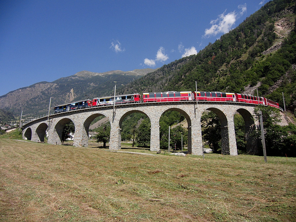 Während der Fotograf dieses Bildes noch eine Fotostelle für das bekannte Motiv der Bernina-Bahn suchte, hatte sich der Mann eines jungen asiatischen Pärchens bereits entsprechend positioniert. Der Bernina-Express D 973 von St. Moritz am 18.08.2012 auf dem Kehrviadukt bei Brusio hat das Ziel Tirano bald erreicht.