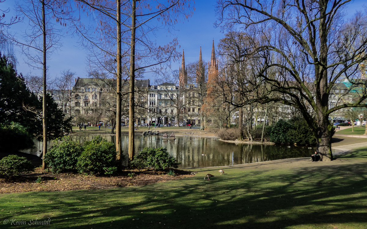 Wiesbaden: Hier blicken wir über den Salzbach-Teich im <u><a href= https://www.wiesbaden.de/leben-in-wiesbaden/freizeit/natur-erleben/gruenanlagen-parks/gruenanlagen-warmer-damm.php  target= _blank >Landschaftspark Warmer Damm</a></u> in Richtung Wilhelmstraße / Innenstadt mit der Marktkirche im Hintergrund. (25.03.2018)