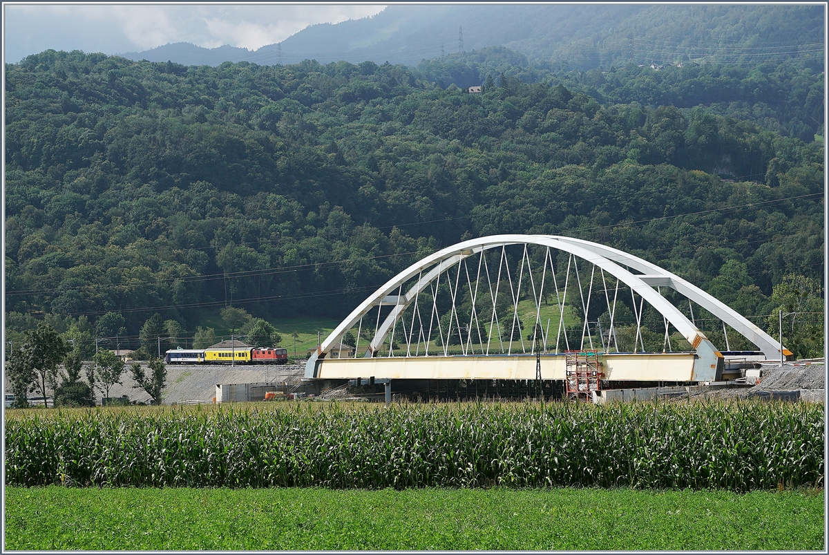 Zwischen Bex und St-Maurice überquert die Strecke Lausanne Birg die Rhone. Die alte Gittereisenbrücke wird nun durch eine sehr gefällige und unübersehbare Neukonstruktion ersetzt. Zu Zeit ist die alte Brücke schon nicht mir in Betrieb und der Verkehr verläuft einspurig über die neue Brücke, wobei vor und nach der Brücke das nördliche Gleis, dann auf der Brücke das Südliche Gleis benutzt wird, so dass die Brücke noch verschoben werden muss. Leider ist es nicht einfach, einen einigermasen guten Fotostandpunkt zu finden.
Auf dem Bild links der Brücke: eine SBB Re 4/4 II mit einem Messzug auf der Fahrt Richtung St-Maurice.
19. August 2016