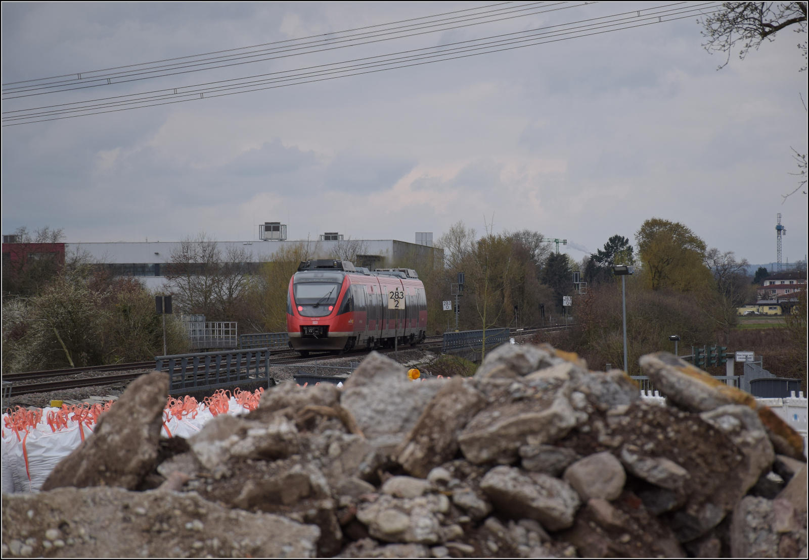 644 040 fährt rheinabwärts über die Autobahnbrücke am Zollhof Rheinfelden. Im Vordergrund die Baustelle des künftigen Haltepunktes Warmbach. März 2026. Bedenklich stimmen vor kurzem angelieferten die Säcke, die in einer Hundertschaft behaupten, sie enthielten Asbest.