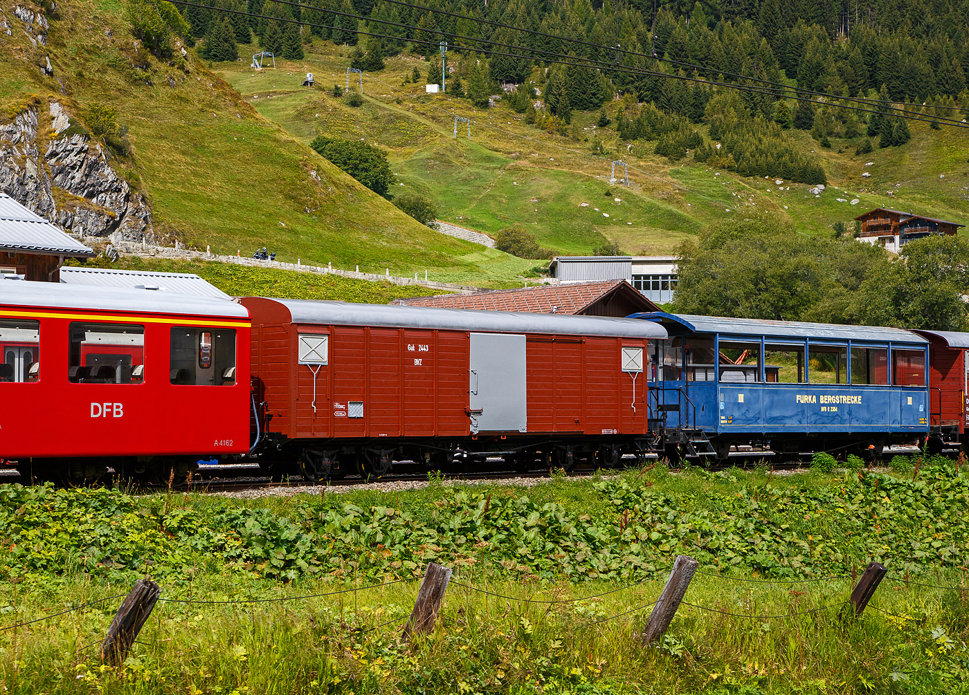 Abgestellt in Realp (Uri) von/bei der DFB Dampfbahn Furka-Bergstrecke AG am 07 September 2021, aufgenommen aus einem fahrenden MGB-Zug heraus:

Links:
Der ehemalige Gterwagen VZ K 63 der Visp Zermatt Bahn, ein schmalspurige vierachsige gedeckter Gterwagen. Der Wagen wurde 1906 von SIG (Schweizerische Industrie-Gesellschaft) in Neuhausen am Rheinfall gebaut und an die damalige VZ- Visp Zermatt Bahn geliefert. 1959 wurde er erst als BVZ K 2423 (Brig-Visp-Zermatt-Bahn), dann doch als BVZ K 2423 gefhrt und 1973 BVZ Gak-v 2443 bezeichnet. Noch vor dem Zusammenschluss am 01. Januar 2003 der BVZ mit der Furka-Oberalp-Bahn (FO) in die heutige Matterhorn-Gotthard-Bahn ging er 2002 als X 4943 zur DFB. Aktuell ist er als DFB X 4921 gefhrt, er dient der Abteilung Zugfrderung und Werksttten (ZfW) als Magazinwagen, ist aber als BVZ Gak 2443 beschriftet.  Wagen hatte ursprnglich 2 Plattformen, der Kasten war ganz aus Holz, 1965 wurde er von SIG umgebaut.

TECHNISCHE DATEN:
Hersteller: SIG
Baujahr: 1906
Spurweite: 1.000 mm (Meterspur)
Lnge ber Puffer : 11.100 mm
Lnge des Wagenkastens: 9.600 mm
Breite: 2.400 mm
Drehzapfenabstand: 6.500 mm
Achsabstand im Drehgestell: 1.400 mm
Eigengewicht:  10,8 t (angeschrieben 11.320 kg)
Ladegewicht:  10 t
Ladeflche: 22,4 m (angeschrieben 19,9 m)
Ladevolumen: 43,0 m
Zul. Hchstgeschwindigkeit: 55 km/h
Bremsen: 	automatische Vakuum- und Handbremse

Rechts:
Der blaue zweiachsige Aussichtswagen C 2354 mit drei Rollstuhlpltzen.  Der Wagen wurde 1892 von SIG (Schweizerische Industrie-Gesellschaft) in Neuhausen am Rheinfall, als dreiachsiger 2.Klasse Personenwagen JS B  1173. fr die damalige Jura-Simplon-Bahn (JS) gebaut und geliefert. Mit der Verstaatlichung der JS zu den Schweizerischen Bundesbahnen (SBB) am 1. Mai 1903 wurde er dann zum SBB Brnig B 223, ab 1920 als C 653 und ab 1994 SBB Brnig X 9954 gefhrt. Im Jahr 1971 wurde er ausgemustert und gin an die VFDK ab 1985 BDB (Ballenberg Dampfbahn) im Jahre 1992 ging er dann an die DFB. Zwischen 1992 und 1995 erfolgte ein Neuaufbau, die Mittelachse wurde entfernt (Achsabstand 6.000 mm), dabei wurde aber jegliche historische Substanz zerstrt. Die Inbetriebnahme bei der DFB erfolgte 1995 als Aussichtswagen C 2354.  Der Aussichtswagen  wurde 2005 von der Wagenwerkstatt Aarau fr drei Rollstuhlpltze und den Rollstuhl-Verlad umgebaut. Der Wagen besitzt Seitenrolls, verglaste Stirnfenster und seitliche ffnungen (herausnehmbare Seitenwandstcke) fr den Rollstuhl-Verlad mittels Hebelift. 

Bereits ab 2020 wurde der Wagen von der DFB zum Verkauf angeboten, ansonsten sollte er verschrottet werden. So ist dies wohl eines der letzten Bilder von ihm, denn er wird aktuell nicht mehr gelistet.

TECHNISCHE DATEN:
Hersteller: SIG
Baujahr: 1892
Spurweite: 1.000 mm (Meterspur)
Lnge ber Puffer: 10.100 mm
Achsstand: 6.000 mm
Eigengewicht 7,1 t
Sitzpltze: 36 und 3 Rollstuhlpltze.
Stehpltze: 16
Beleuchtung: elektrisch ab Batterie
Heizung: Durchgang
Bremsen: Vakuum- und Handbremse
Bemerkung: letzte Revision R1 Mai 2017	
