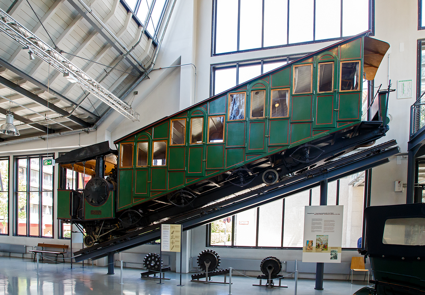 Bhm 1/2 Zahnrad-Dampftriebwagen Nr.10 der Pilatus Bahn ausgestellt im Verkehrszentrum des Deutschen Museums in München (Theresienhöhe), hier am 16.06.2018. Leihgabe der Pilatus Bahnen.

Der Dampftriebwagen wurde 1900 von der SLM unter der Fabriknummer 1309 gebaut und an die Pilatus Bahn geliefert.

Mit Seilbahnen und Zahnradbahnen eroberten Touristen und Ausflügler am Ende des 19. Jahrhunderts die Einsamkeit der Berge. Als erster Schweizer Berg erhielt der sanfte Rigi 1875 die erste Bergbahn Europas. Nach dessen erfolgreicher Eroberung galt es dem schroffen und sagenumwobenen Pilatus am Vierwaldstätter See mit einer Bergbahn zu Leibe zu rücken. Eine besondere technische Herausforderung stellte dabei die starke Neigung der bevorzugten Trasse dar.

Eduard Locher entwickelte dafür 1888 ein Zahnstangensystem. Dank der liegenden Anordnung seiner Fischgrätenzahnstange und dem horizontalen Zahneingriff mit dem liegenden Zahnradpaar war eine Steigung von 48 % realisierbar.

Am 4. Juni 1889 dampfte der erste fahrplanmäßige Zug zum Pilatus. Er brauchte für die 4,3 Kilometer lange Strecke 70 bis 80 Minuten. Bereits 1895 reisten 40.000 Besucher per Zahnradbahn auf den Pilatus. Neun Dampftriebwagen waren dafür im Einsatz. Später kamen noch die Triebwagen 10 (1900) und 11 (1909) hinzu..

Die Triebwagen versahen größtenteils bis zur Umstellung auf elektrischen Betrieb im Jahre 1937 ihre Dienste. Mit den elektrischen Triebwagen konnte man mit weniger Personal in kürzerer Zeit mehr Gäste befördern. Bis auf die Dampftriebwagen 9 und 10 wurden die restlichen Fahrzeuge noch im selben Jahr verschrottet. Wagen 9 blieb bis 1981 als Reserve bei der Pilatusbahn und ist seitdem im Verkehrshaus der Schweiz in Luzern ausgestellt, Wagen 10 ist eine Dauerleihgabe des Verkehrshauses an das Deutsche Museum in München.

Heute fahren jährlich über 250.000 Besucher mit der steilsten Zahnradbahn der Welt auf den Pilatus, um von hier einen Blick auf die Schweizer Alpenwelt zu werfen.

TECHNISCHE DATEN:
Spurweite:  800 mm
Achsformel:  2z
Länge über Puffer: 10.300 mm
Achsabstand der Laufräder: 7.200 mm
Leergewicht: 7,6 t 
Dienstgewicht:  13,2 t
Kohlevorrat: 500 kg
Wasservorrat: 880 l
Höchstgeschwindigkeit: 3,6 km/h (bergwärts) / 3 km/h (talwärts)
Leistung: 73 PS
Treibzahnraddurchmesser:  409 mm
Zahnradsystem:  Locher
Zylinderdurchmesser:  235 mm
Kolbenhub: 300 mm
Kesselüberdruck: 12 bar
Anzahl der Heizrohre:  130
Rostfläche:  0,40 m²
Strahlungsheizfläche:  2,40 m²
Verdampfungsheizfläche:  21,0 m²
Steigung max.:  48 %
Sitzplätze:  35
